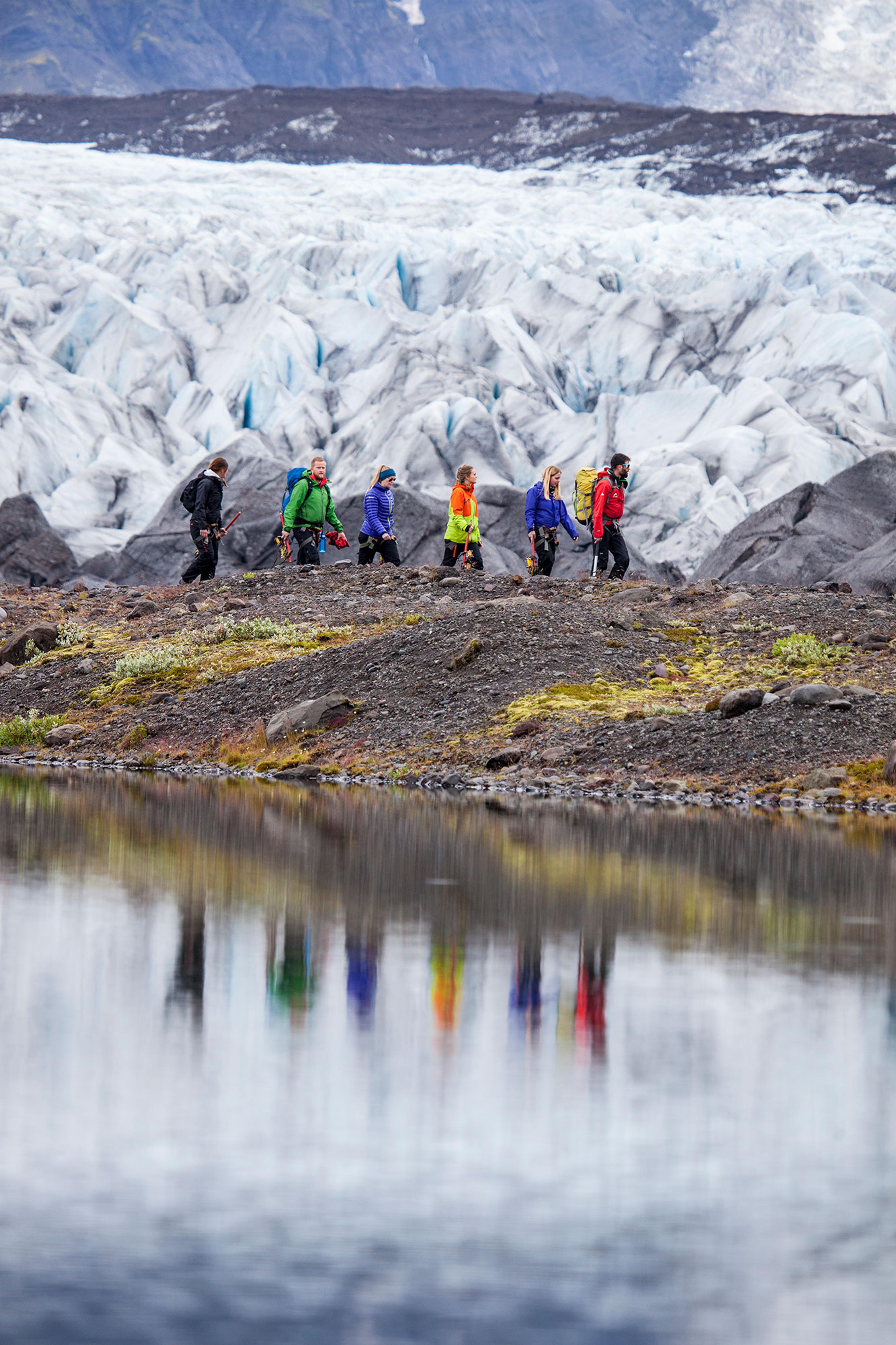 Hikers next to Svinafellsjokull reflect in the water on their glacier walk trip.