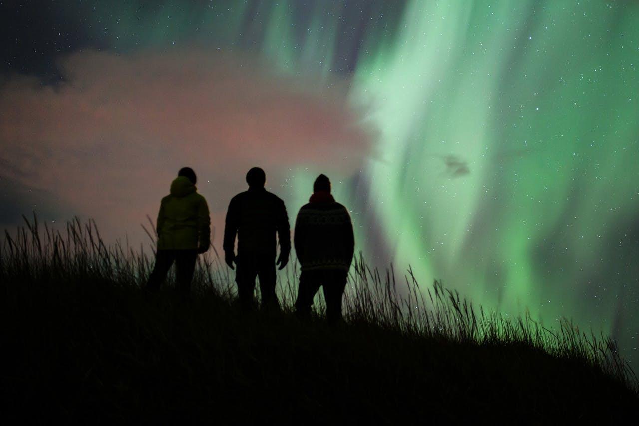 Northern lights in the sky over three silhouettes of people