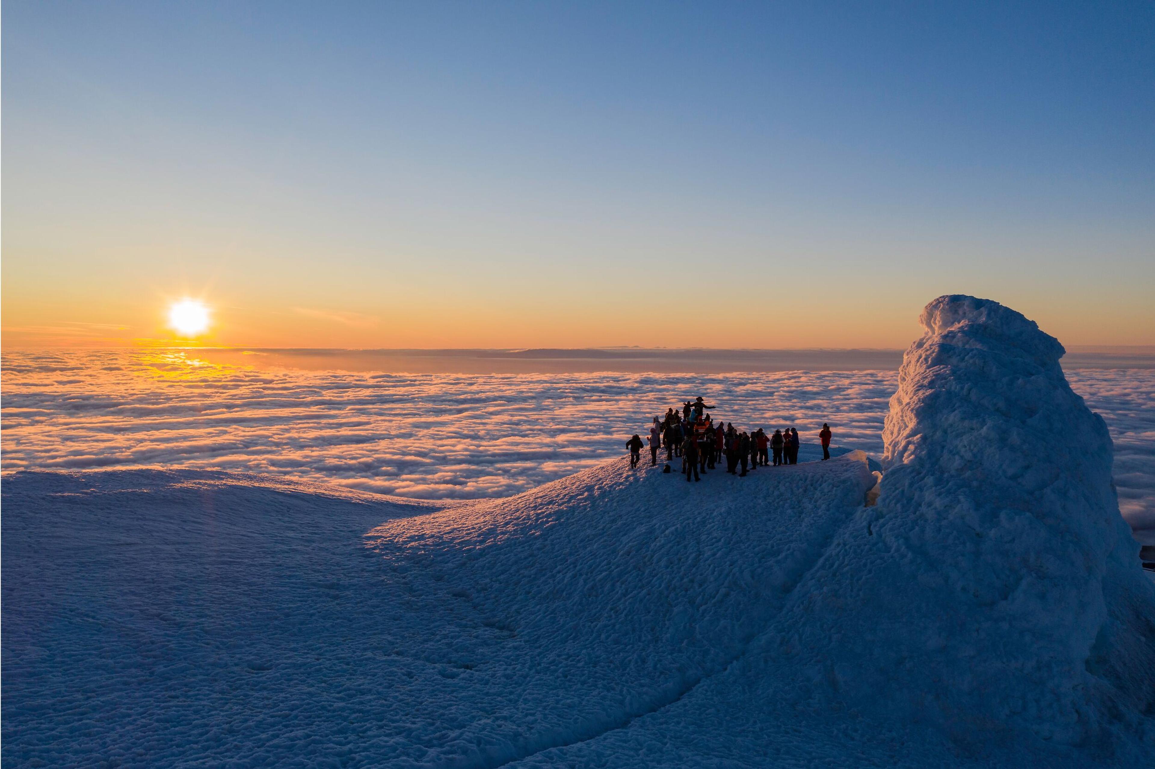 A group of people standing at the Snæfellsjökull summit and sunrise or sunset