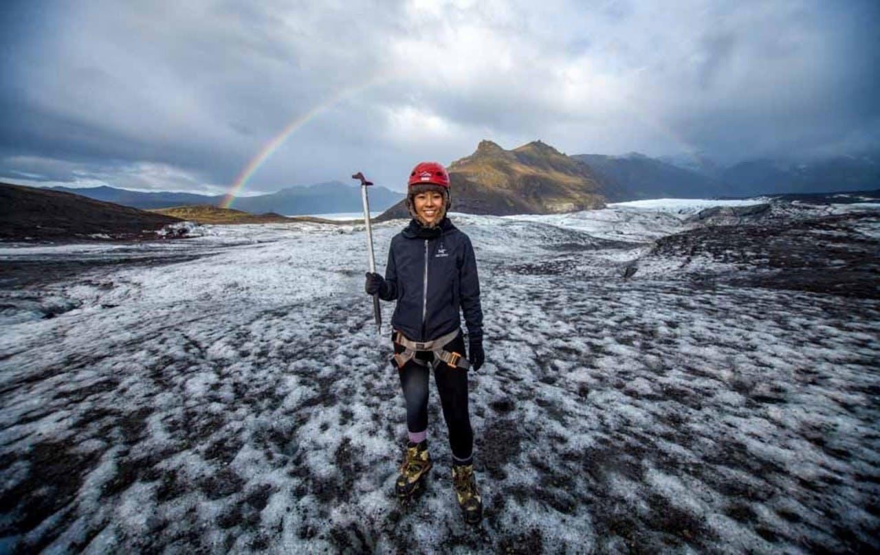 Woman on Sólheimajökull with a rainbow above