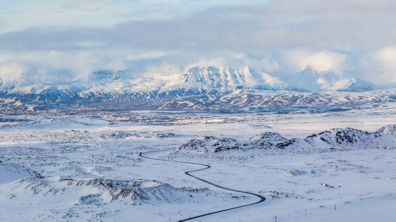Landscape photo of snow-covered mountains hidden by clouds and a road leading up to them