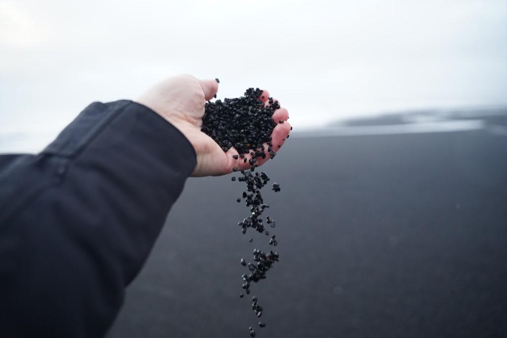 A hand holding a handful of black sand with the beach in the background