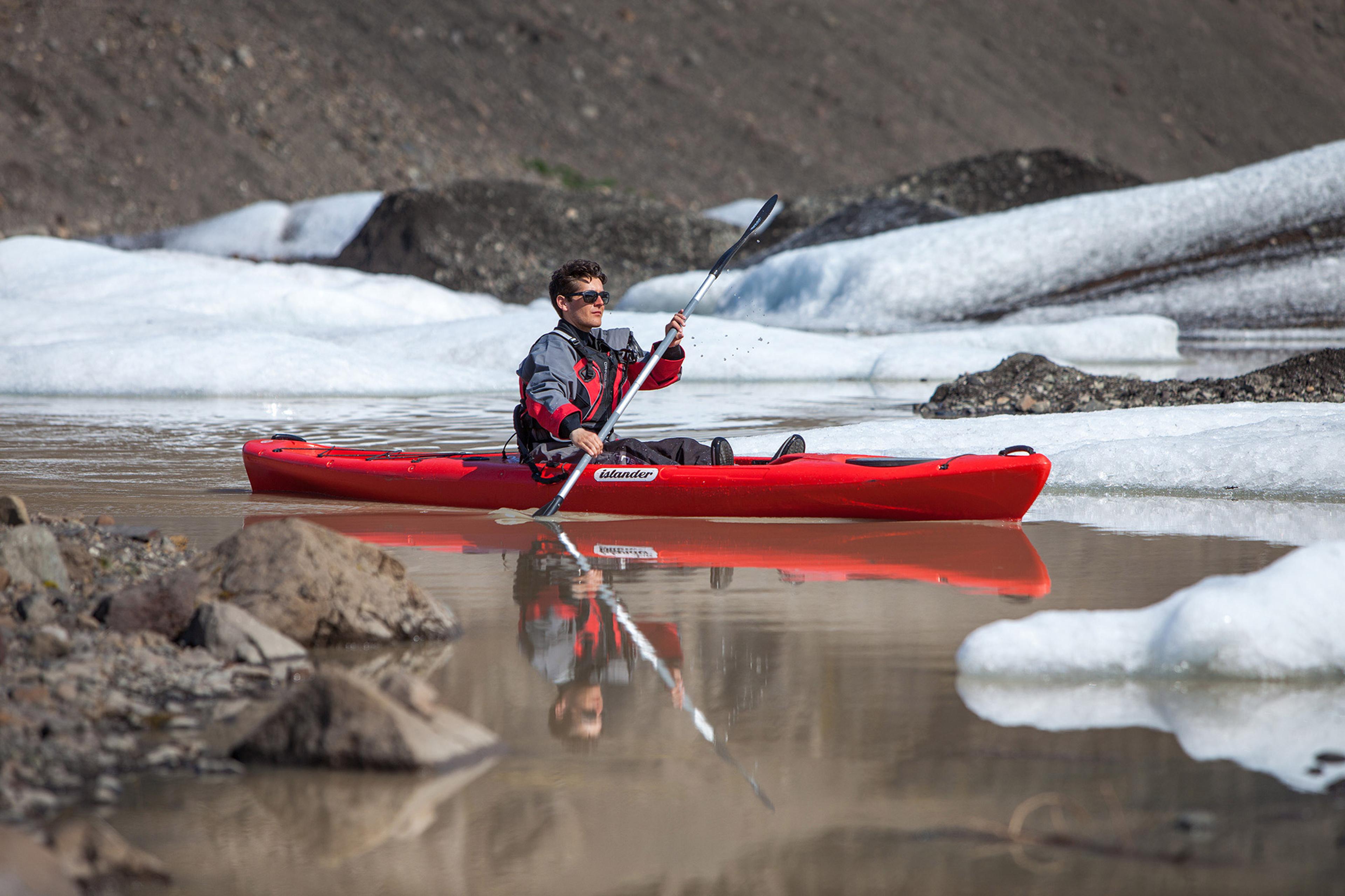 A person paddling in a red kayak on Solheimajokull’s calm glacier lagoon in Iceland