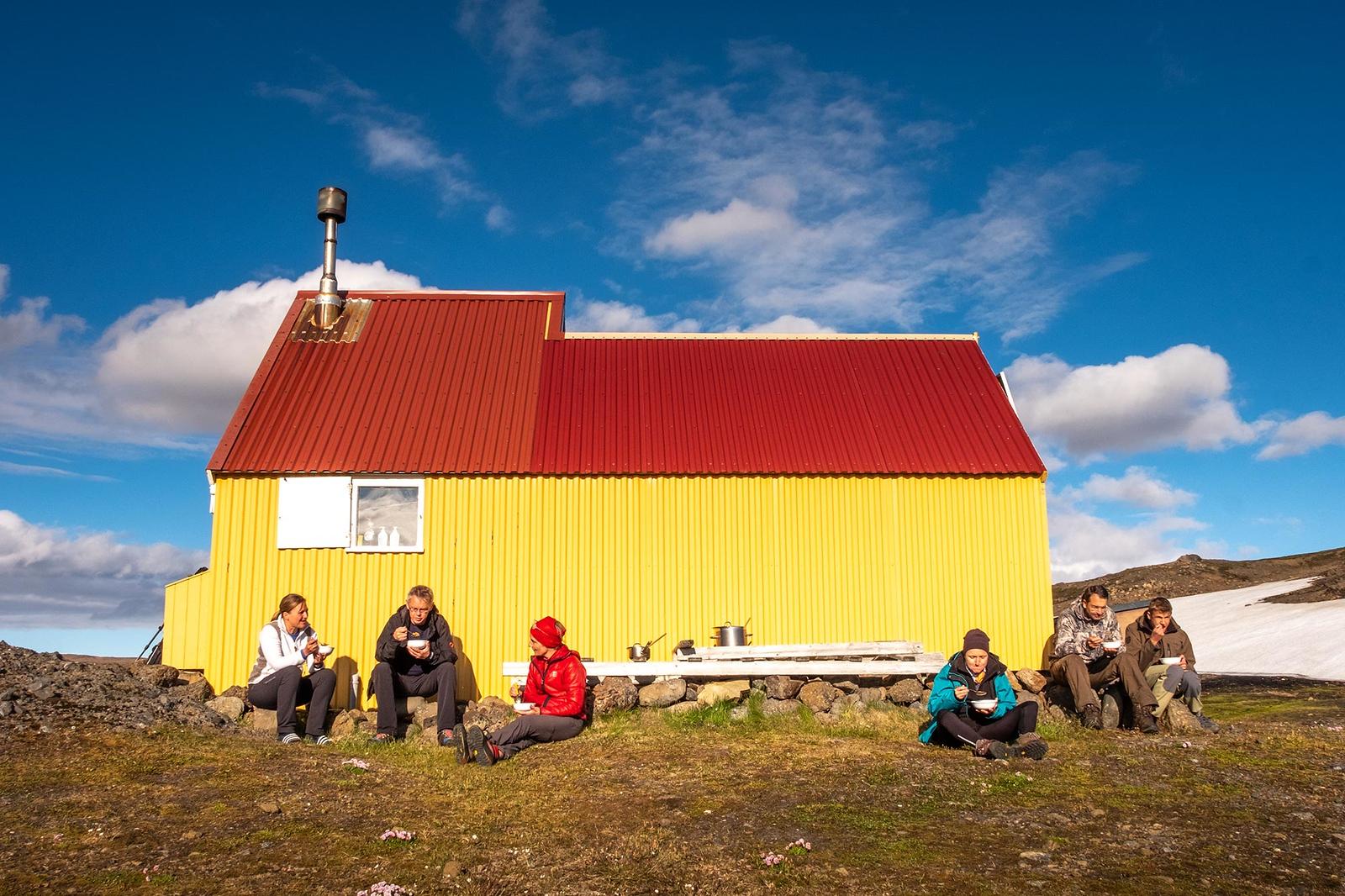 People sitting outside a bright yellow mountain hut eating