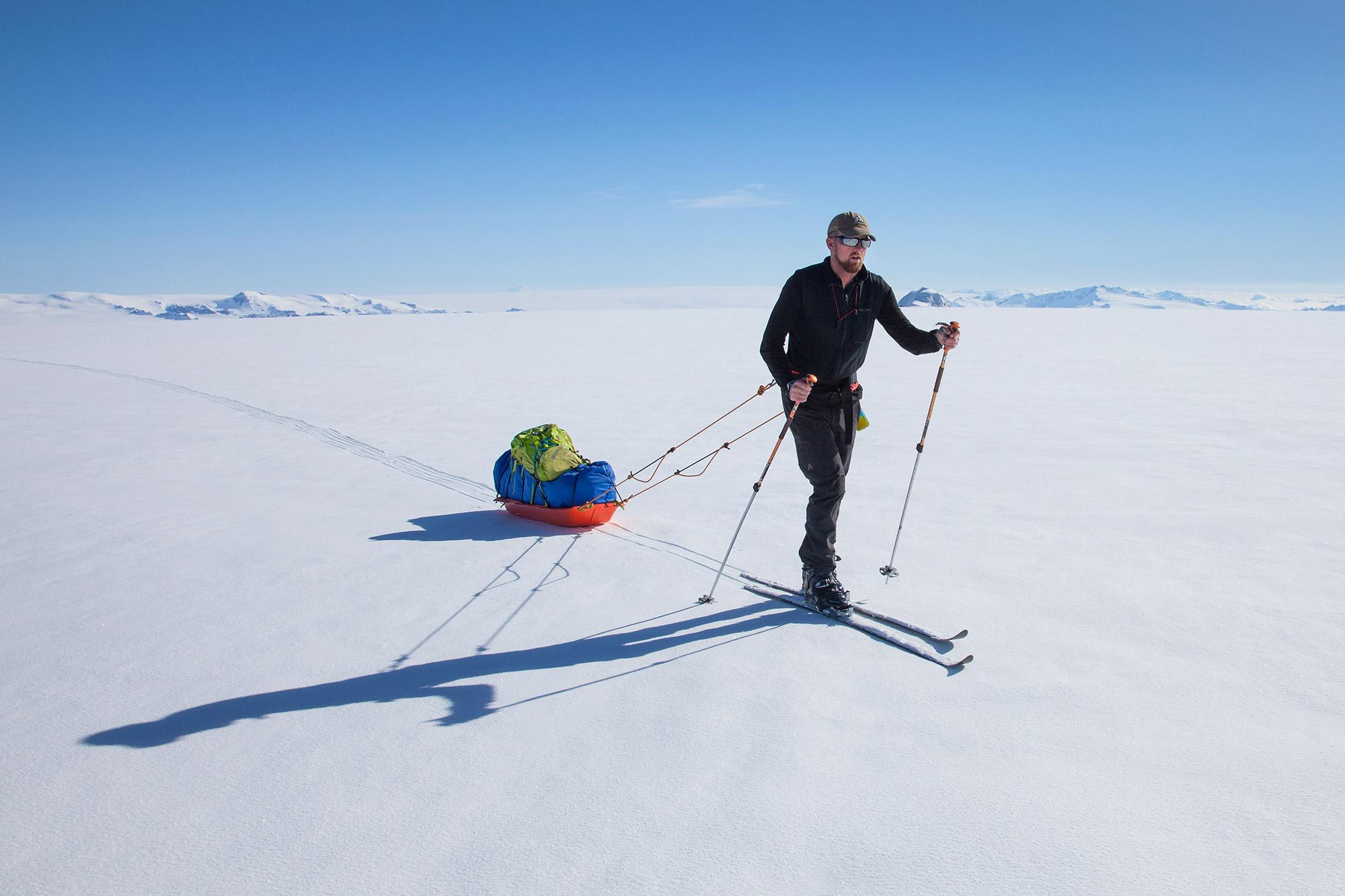 A guide skiing in the sunshine on the glacier pulling a pulka behind him