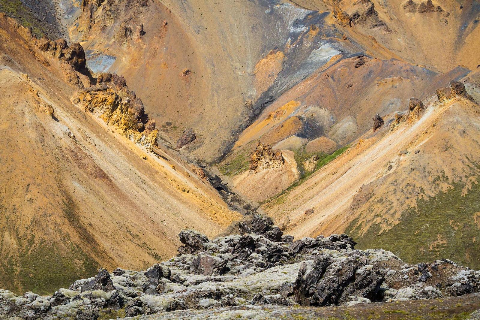Yellow and steep mountains behind a rocky hill covered in moss