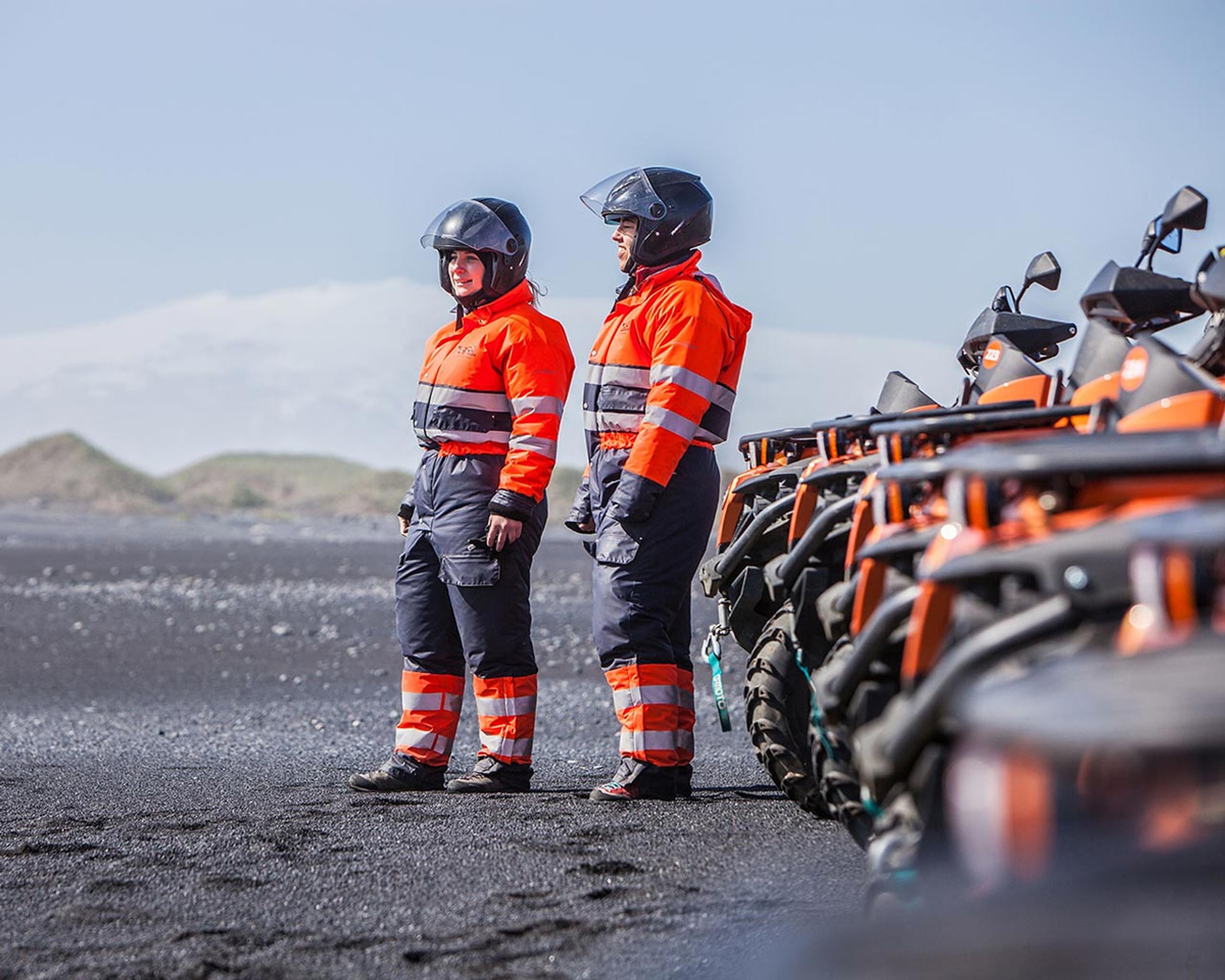 Two girls standing in front of many atv quad bikes pon a black sand