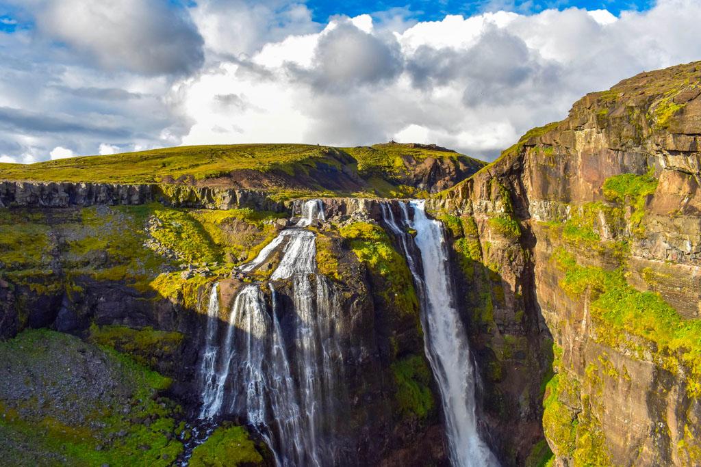 Waterfall cascades into a deep gorge surrounded by green scenery