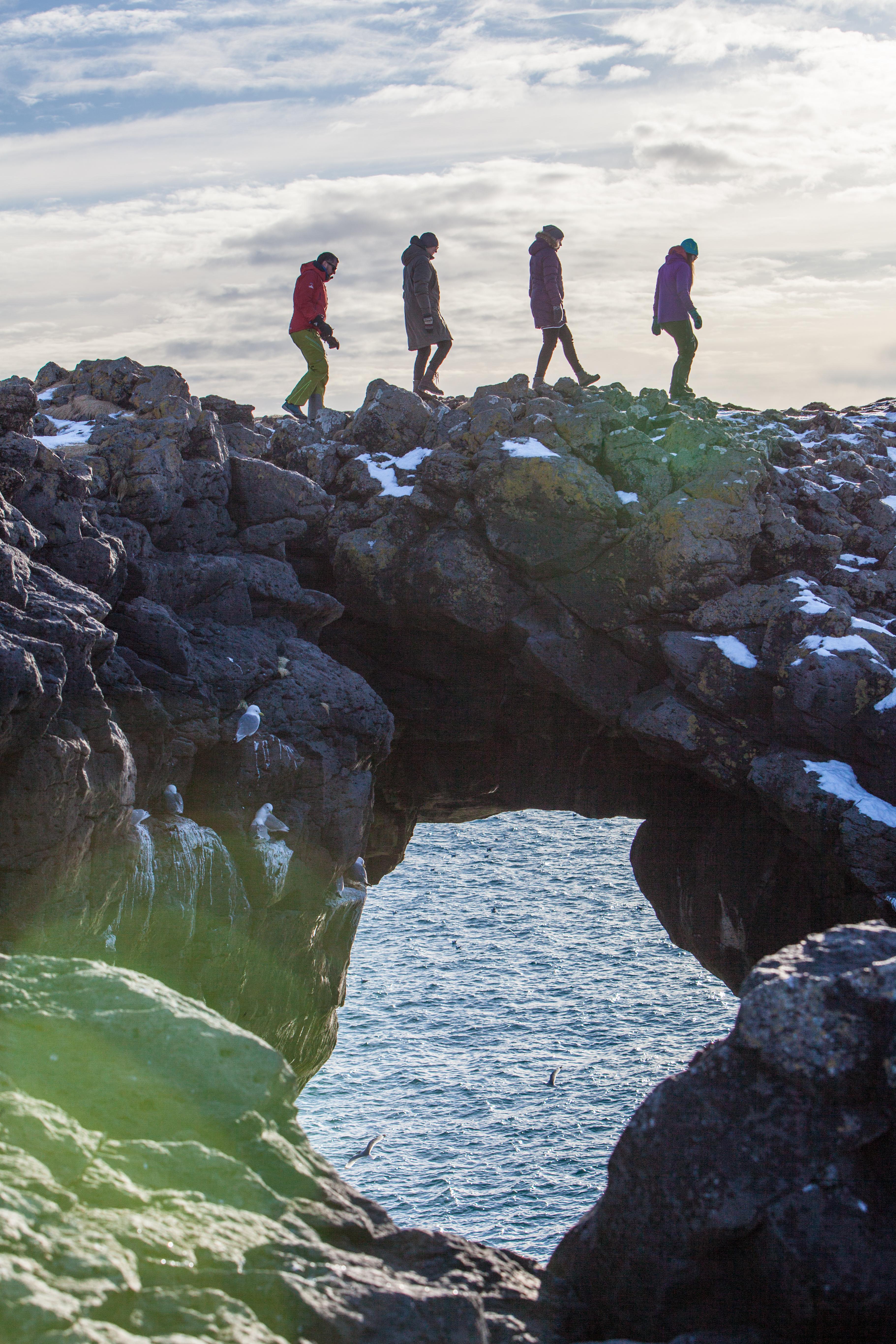 People walking on a rock arch At Arnarstapi