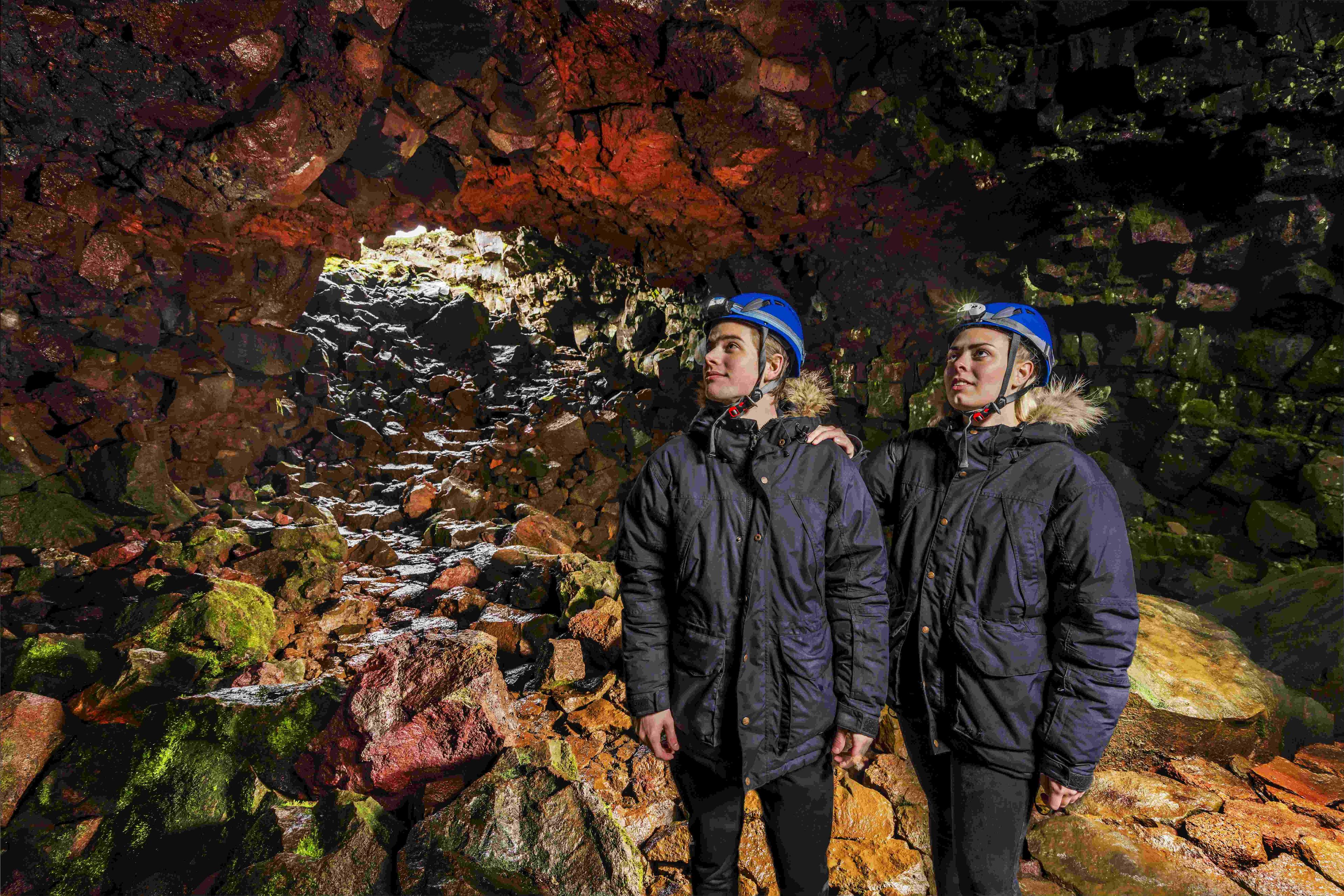 A couple in black jackets with blue helmets admiring the rock formations inside the lava tunnel.