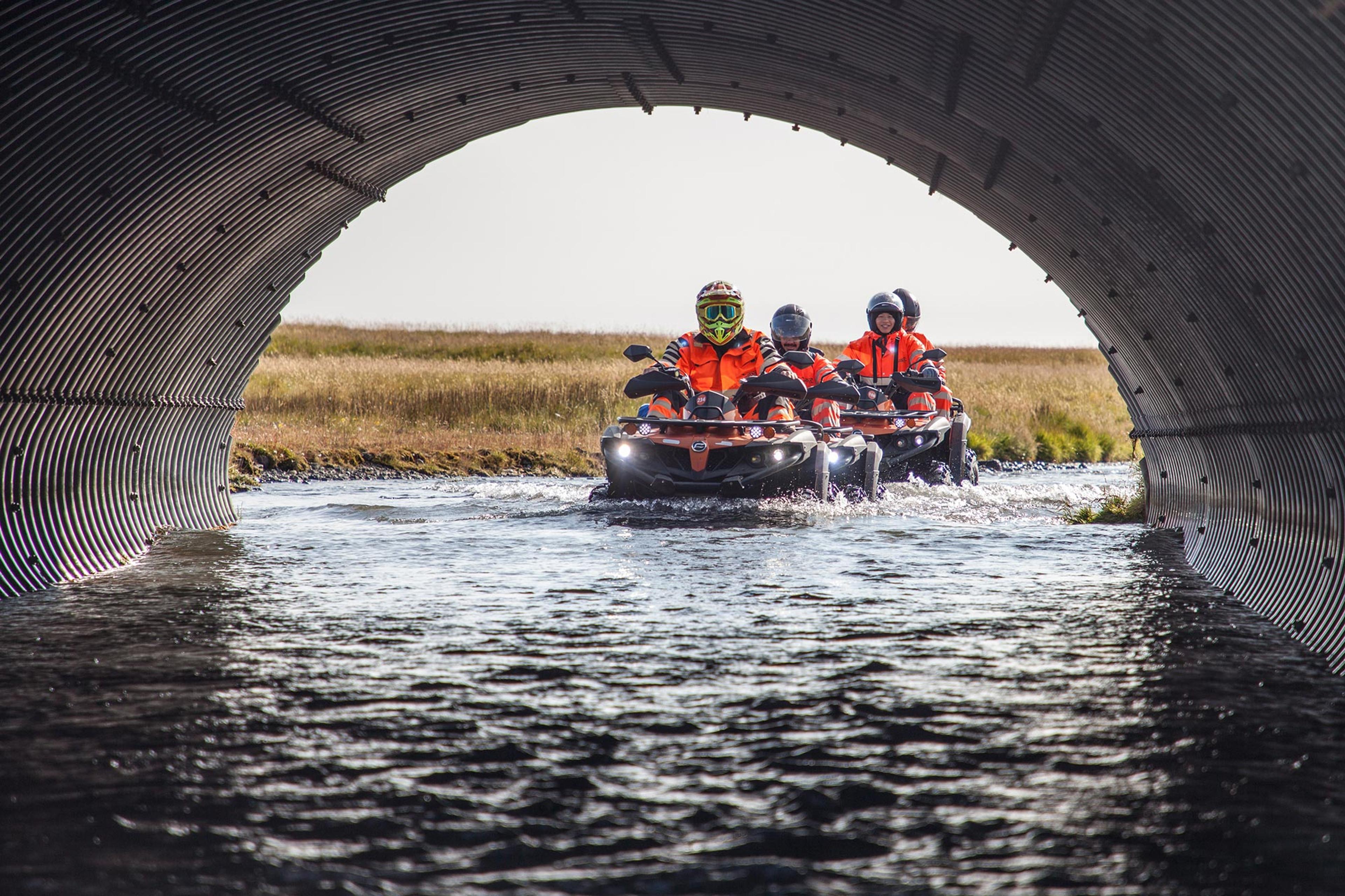 Group of ATV quad bike drivers going under a road through a bi metal tube where water flows