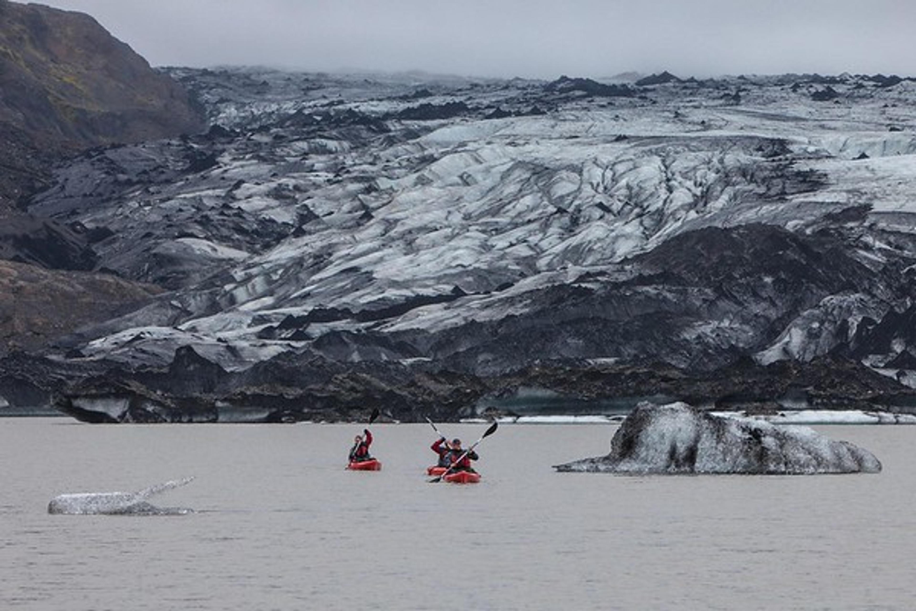 The mighty Sólheimajökull outlet glacier in the background as kayaks go by on the lagoon