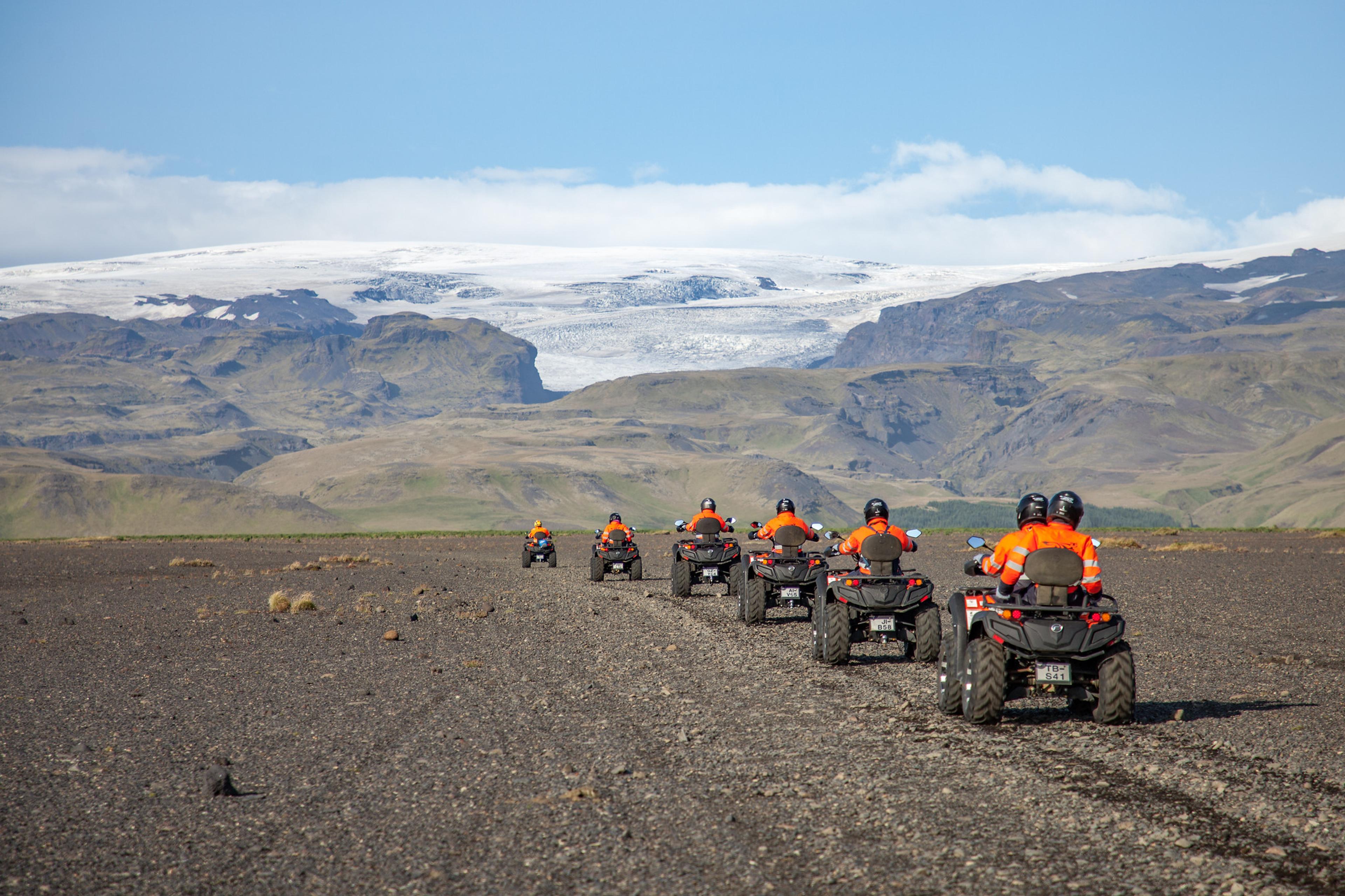 Awesome glacier backdrop as the group of atv riders go by the sandy area of Sólheimasandur