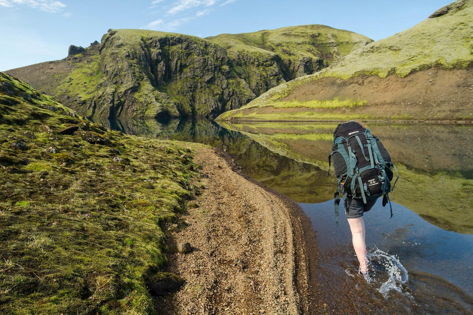 A woman walking in the water surrounded by beautiful mountains covered in nature growth
