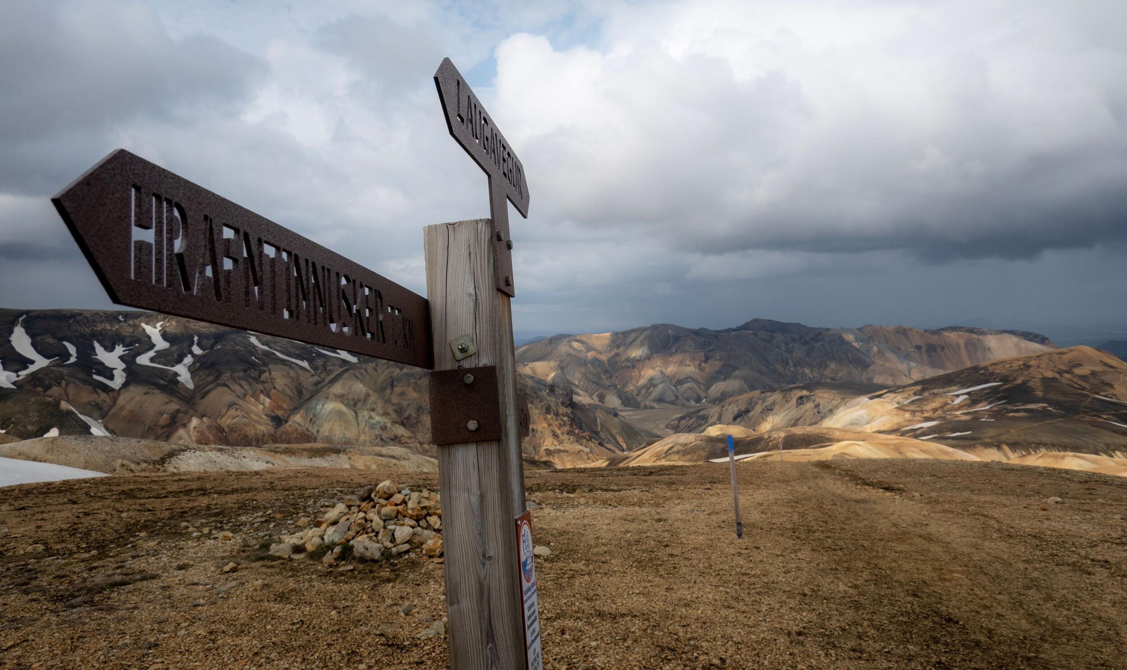 A sign post saying "Hrafntinnusker" and "Laugavegur" with rhyolite mountains in the background