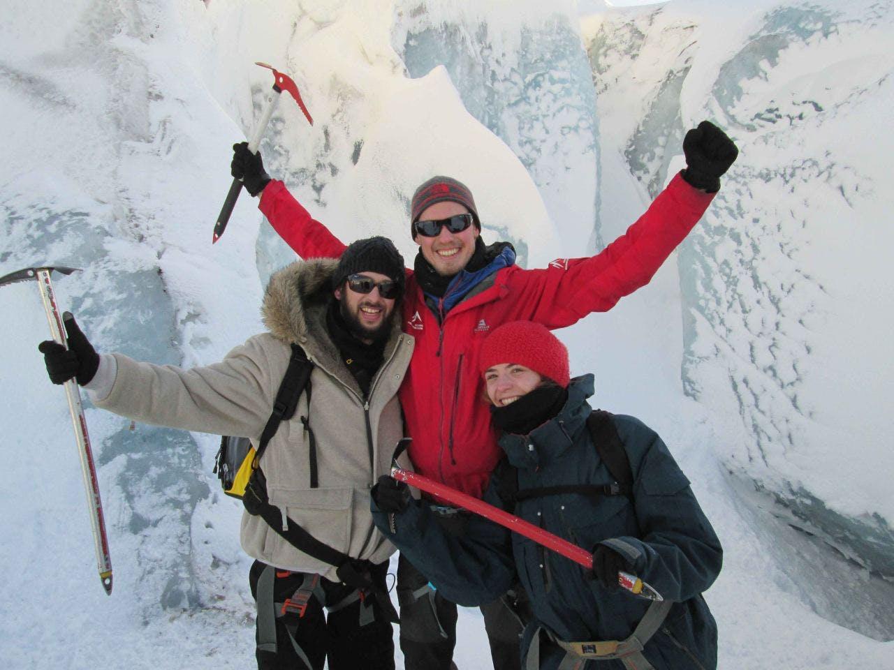 Three people with ice-axes standing in front of snowy ice