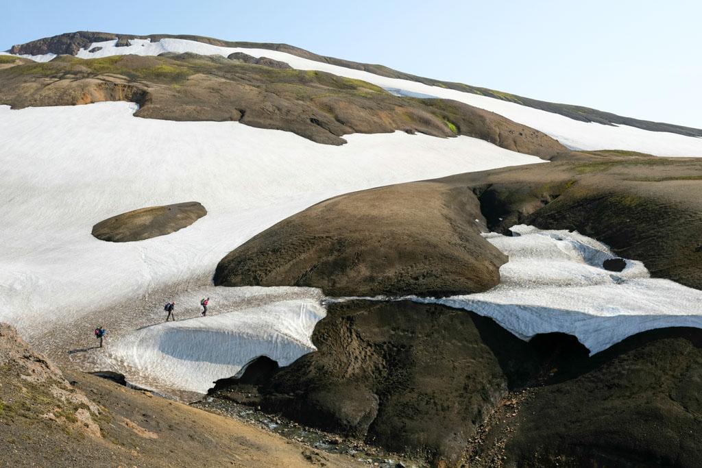 Hikers walking through patches of snow and rugged terrain in Fjallabak Nature Reserve, Iceland.