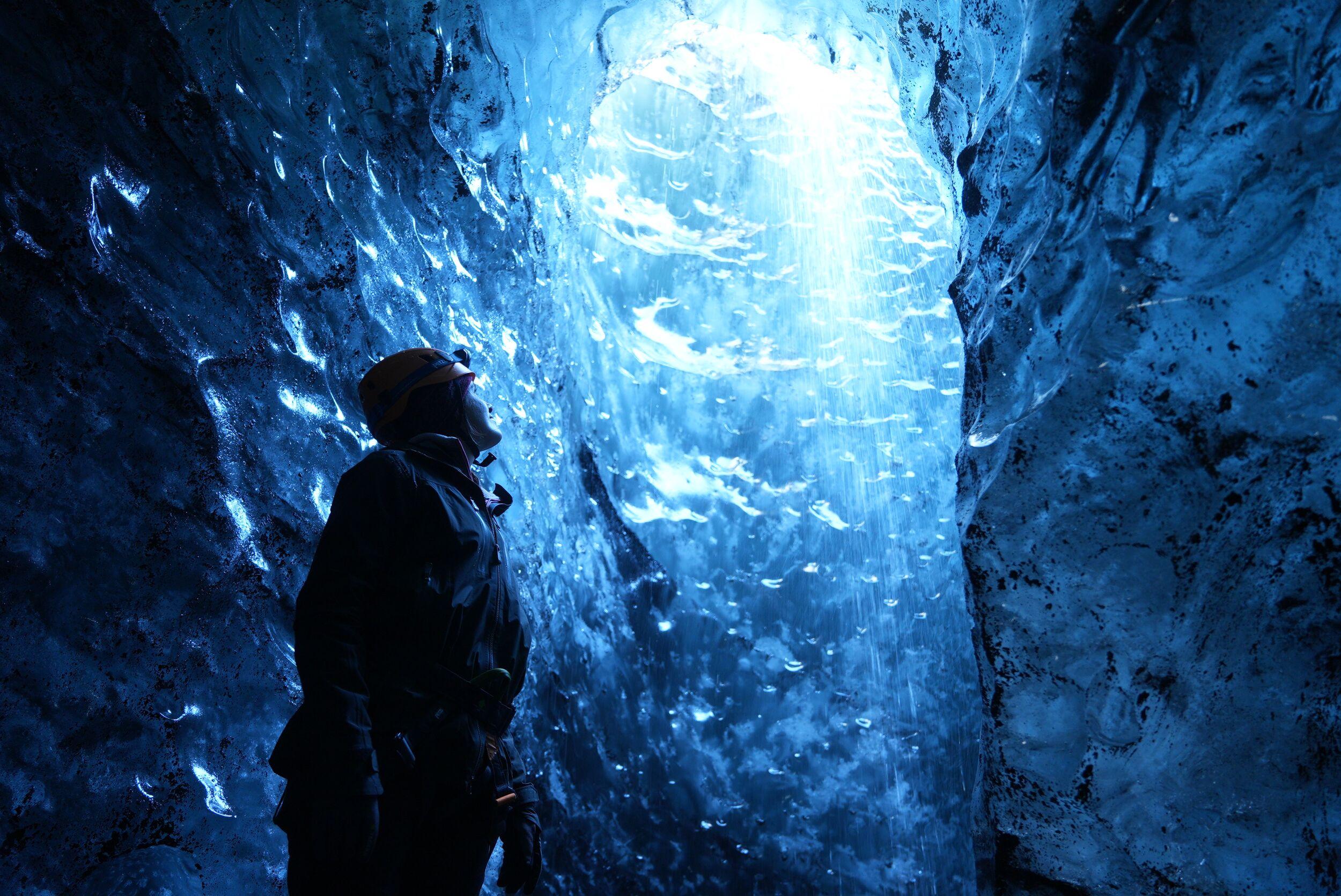 A person looking up at a block of ice within an ice cave