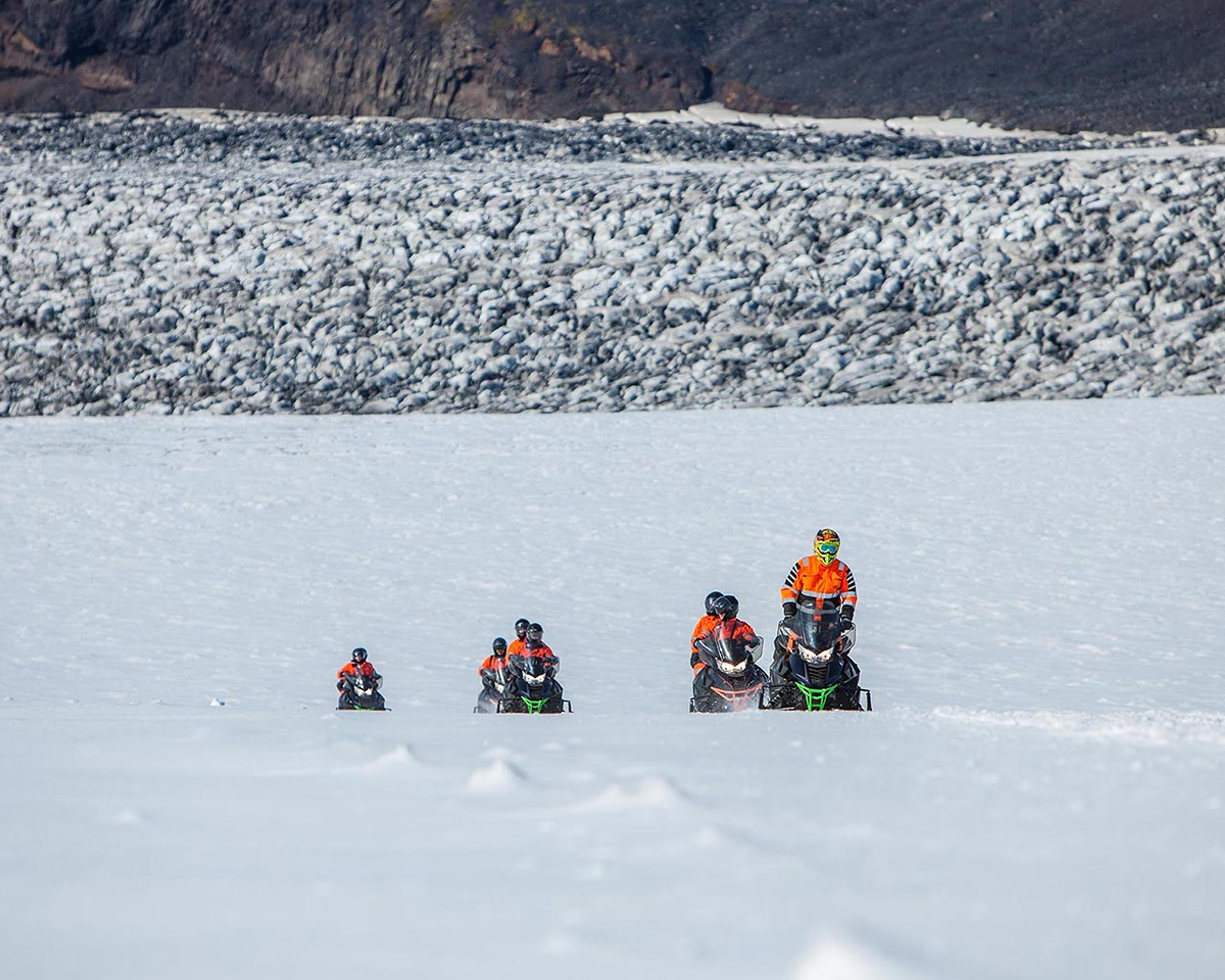 Group of snomobiles going towards the top of the glacier. A crevassed area in the background.