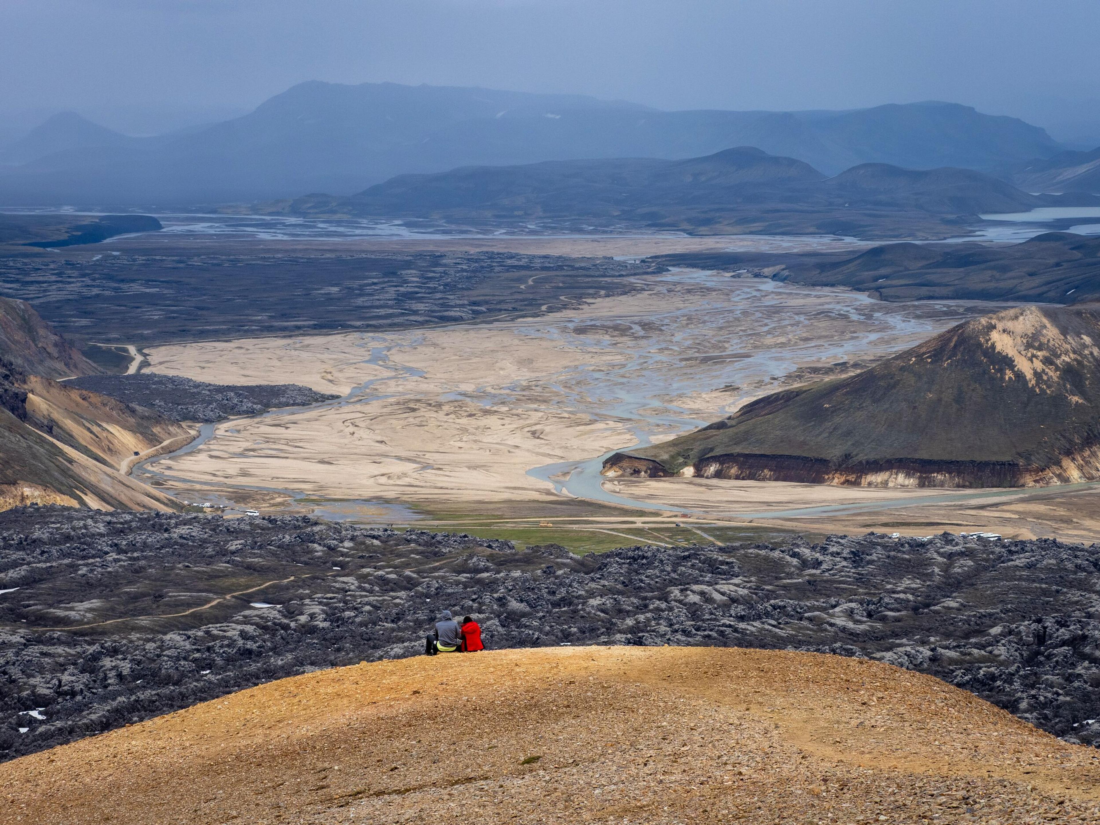 Travellers sat observing the flooded desert plains below with misty mountains in the background