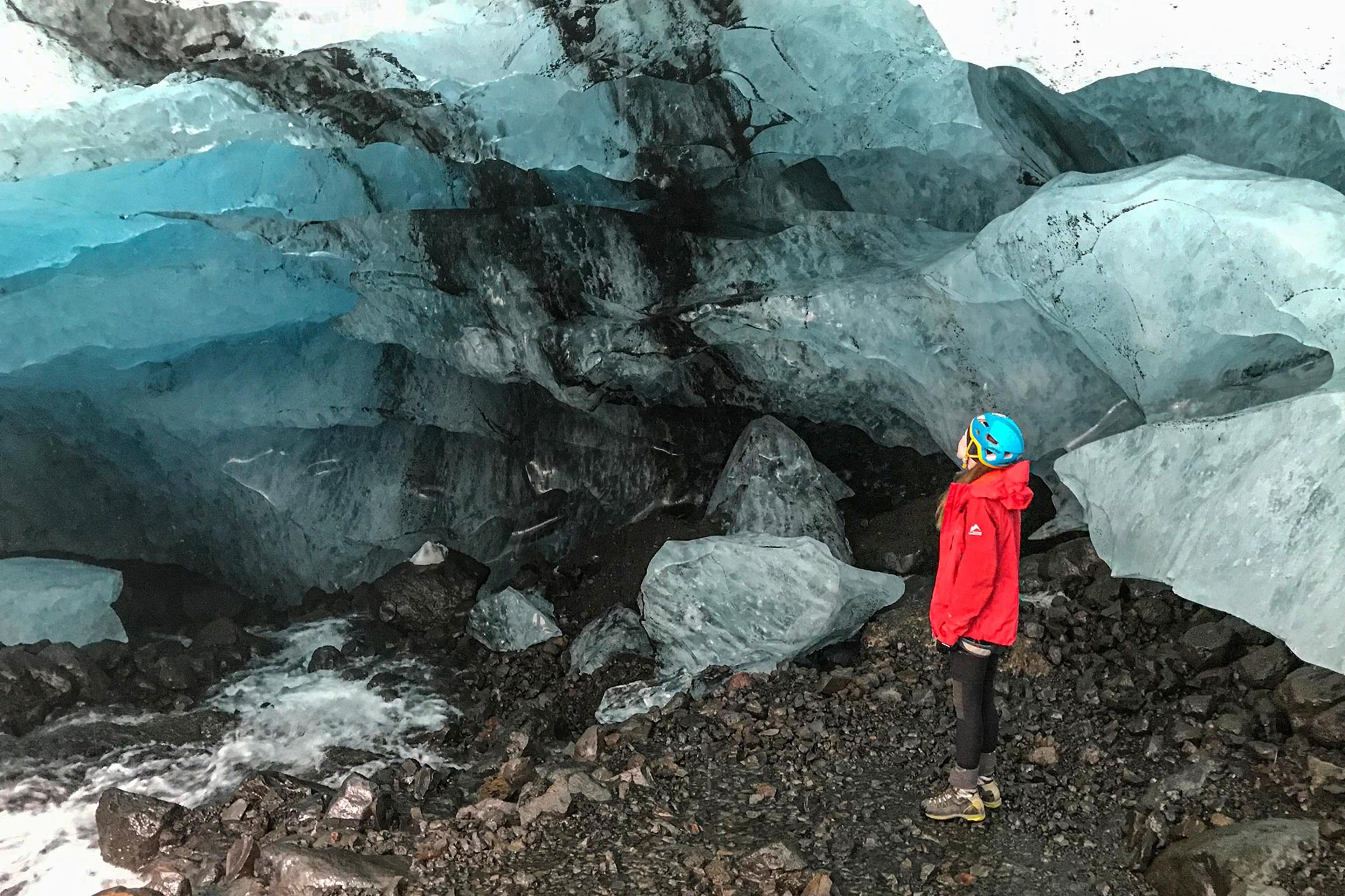 A girl in a red jacket and a blue helmet looking at a blue ice