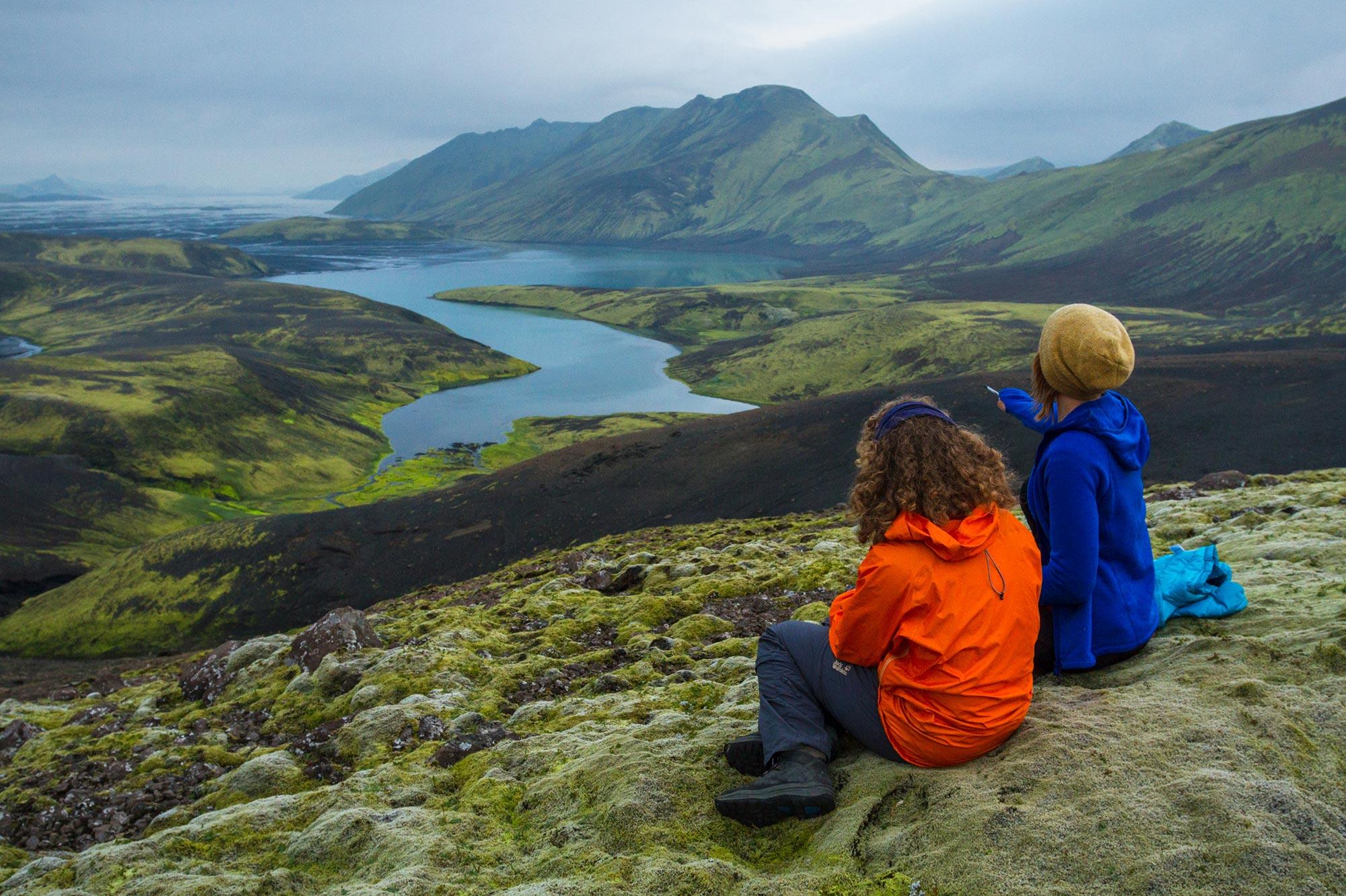 Man and a woman seen from the back looking over a river and mountains in Iceland