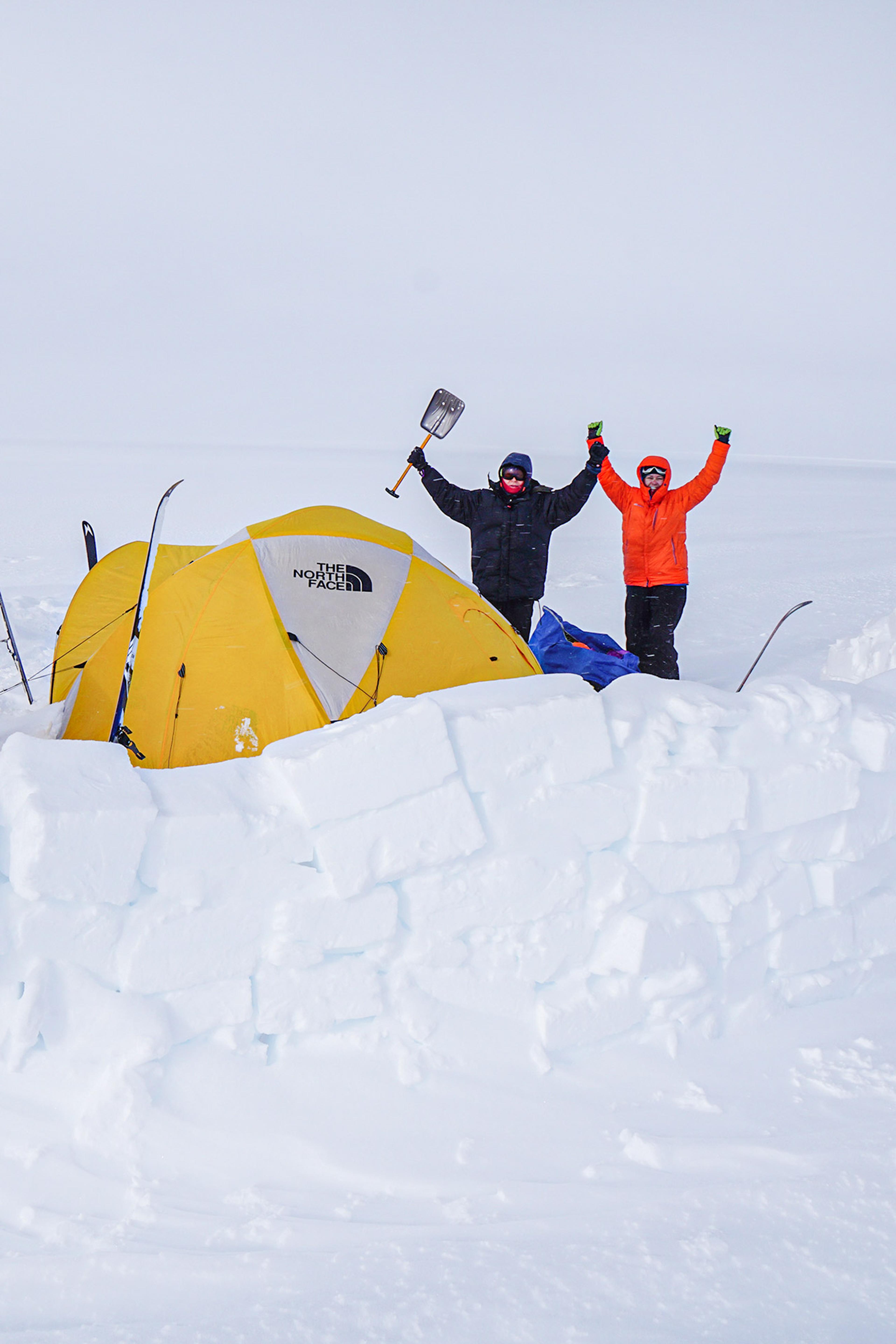 Happy people by their tent and protective snow wall