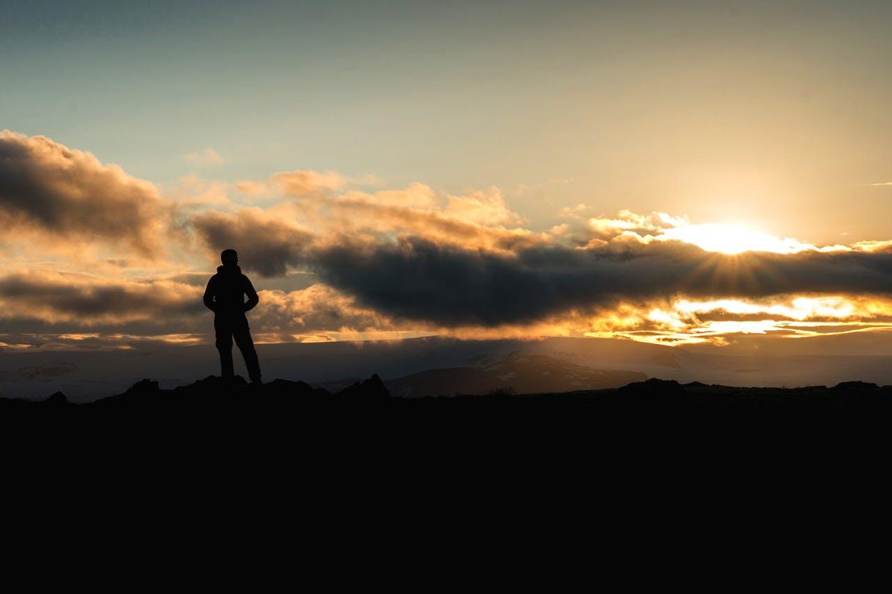 man standing looking over orange sunrise