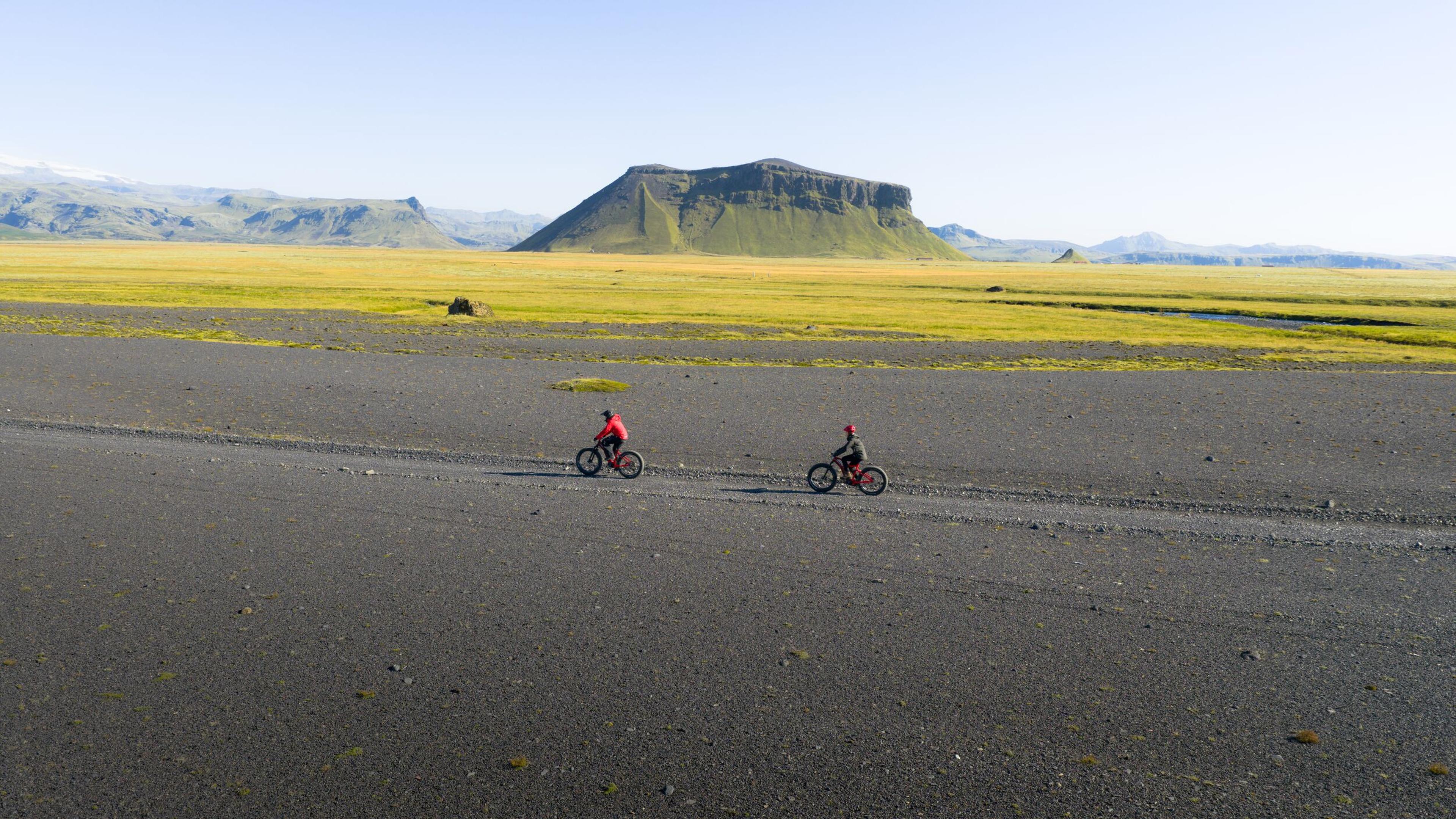 two people riding a bike on a sand with mountain in back