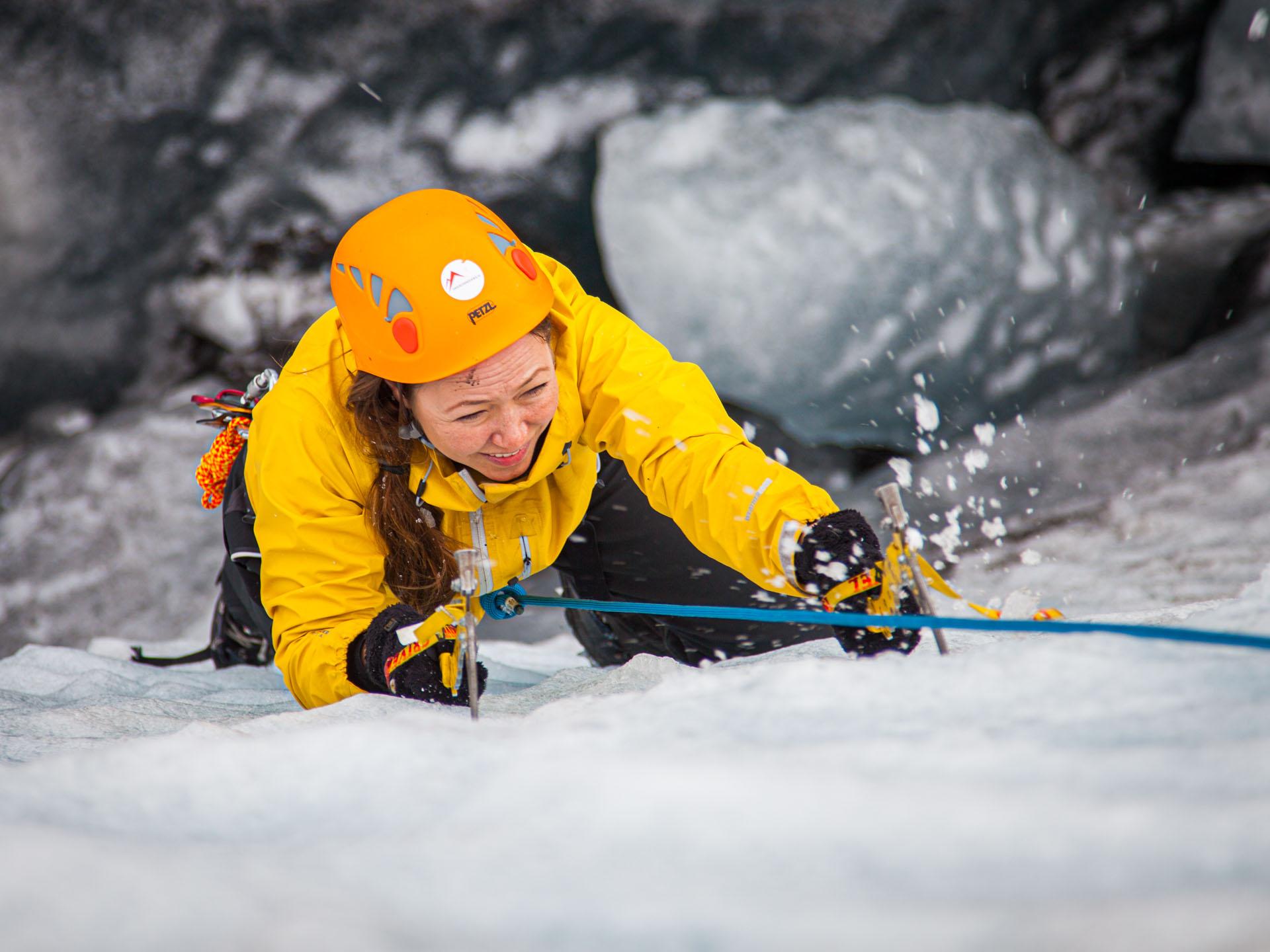 A woman climbing up a glacier with ice picks