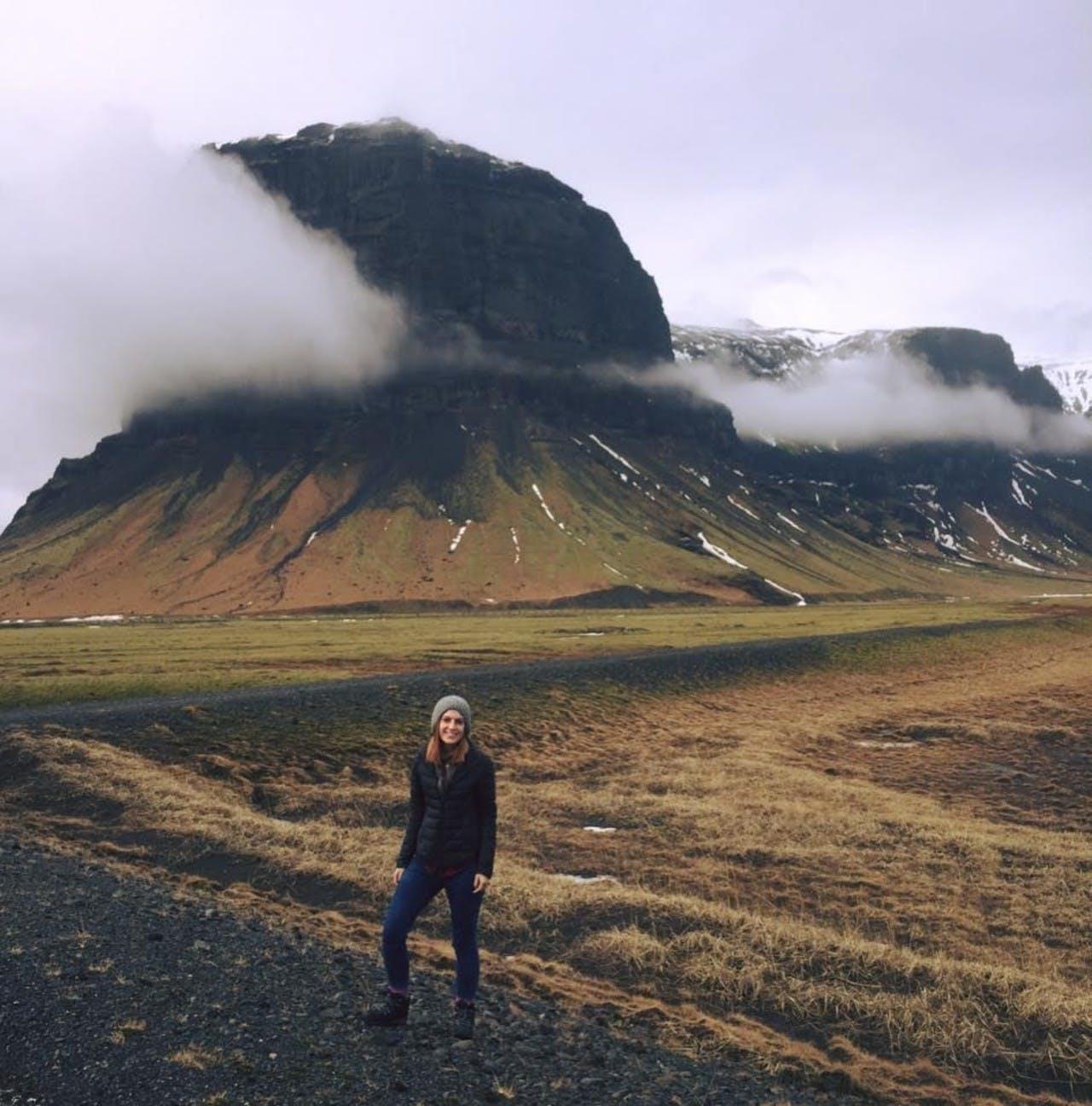A person standing in front of a the mountain Lómagnúpur on a cloudy day
