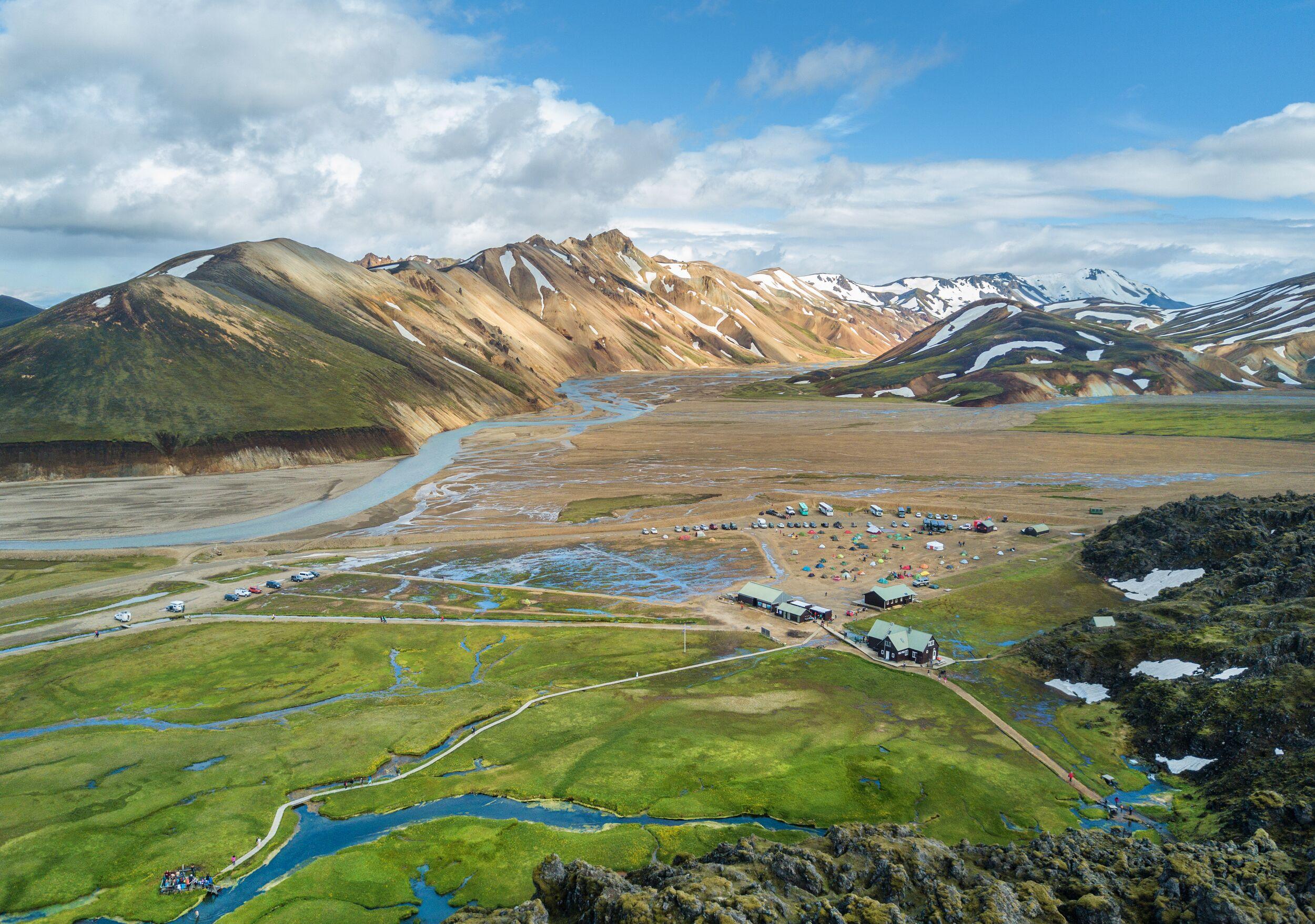 Aerial view of Landmannalaugar's base camp, with colorful rhyolite mountains, green fields, and winding streams stretching across the valley.