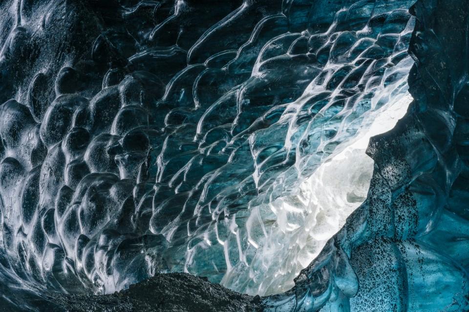 "A close-up view of the textured surface of glacial ice, with deep blue and white hues creating a marbled effect. The intricate patterns suggest the dynamic nature of the ice as it forms and melts over time.