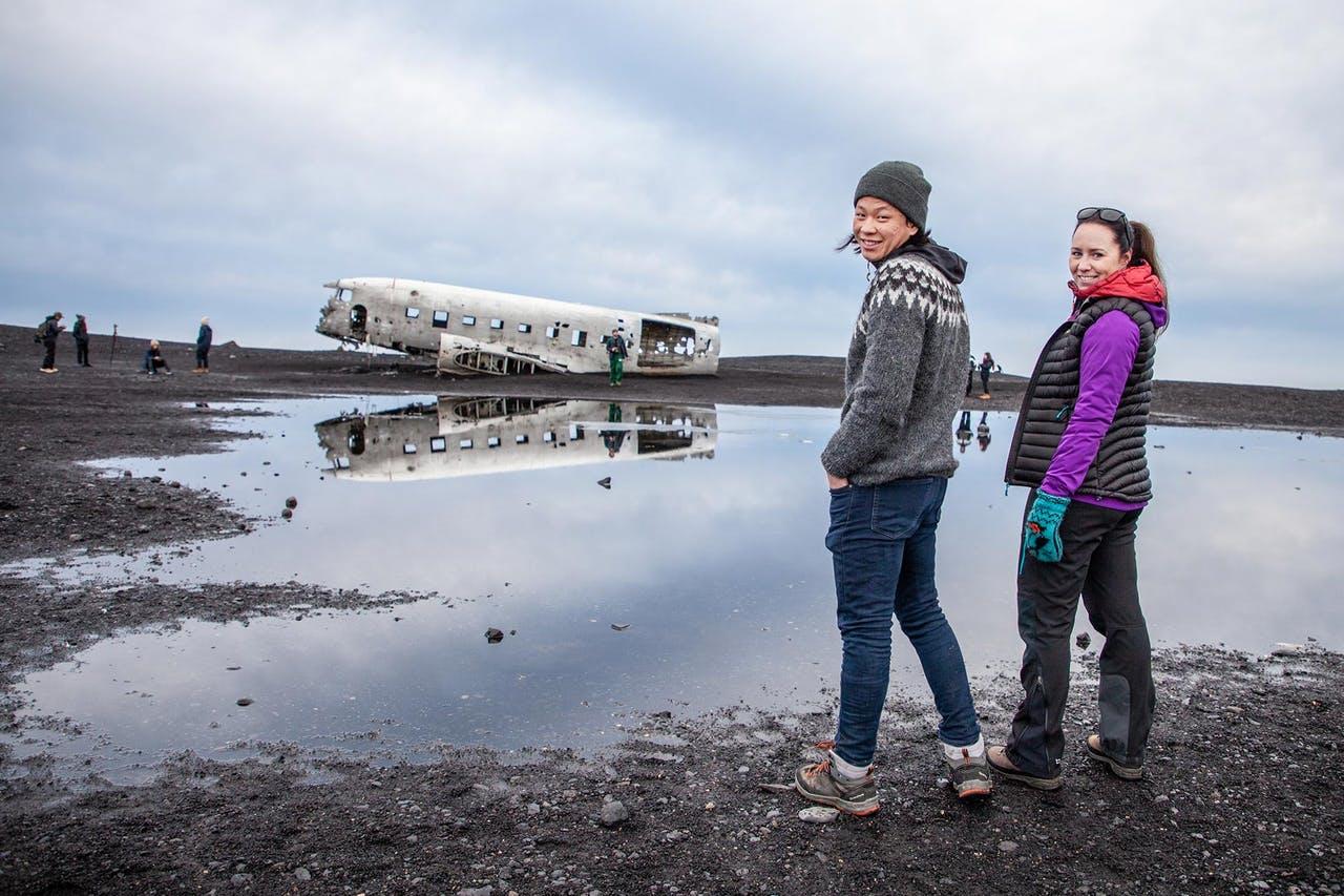 Two people looking back, standing in front of the DC-3 plane wreck in Iceland in May