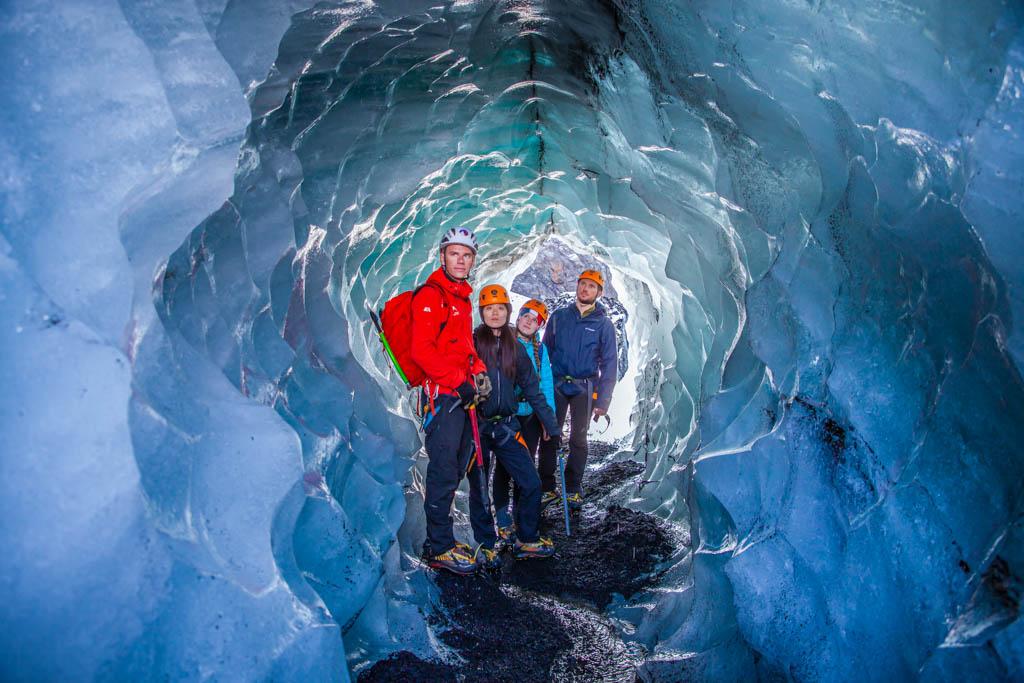 A group of glacier hikers posing for a picture at the entrance of a small ice cave
