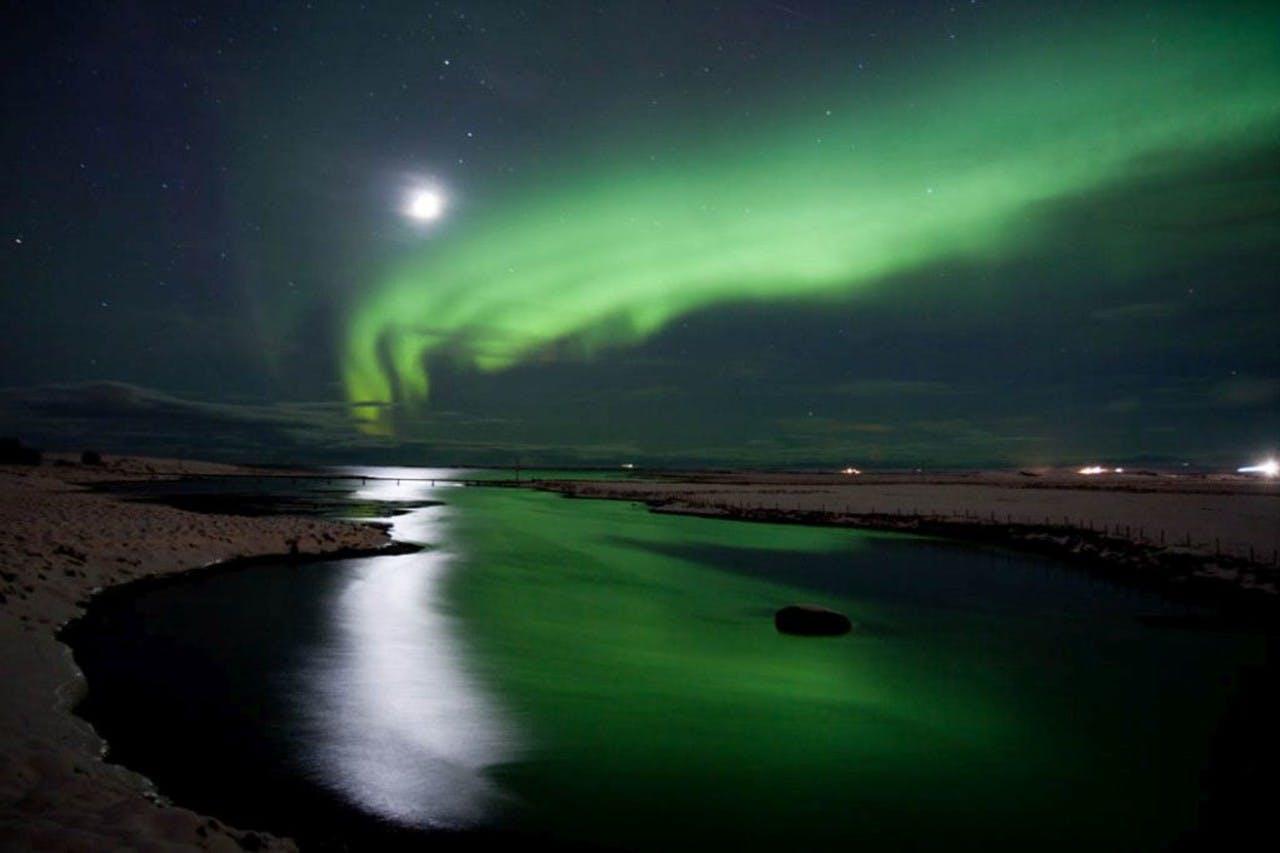 Beautiful bright green Northern Lights dancing in the sky and reflecting in lake it is winter time in Iceland