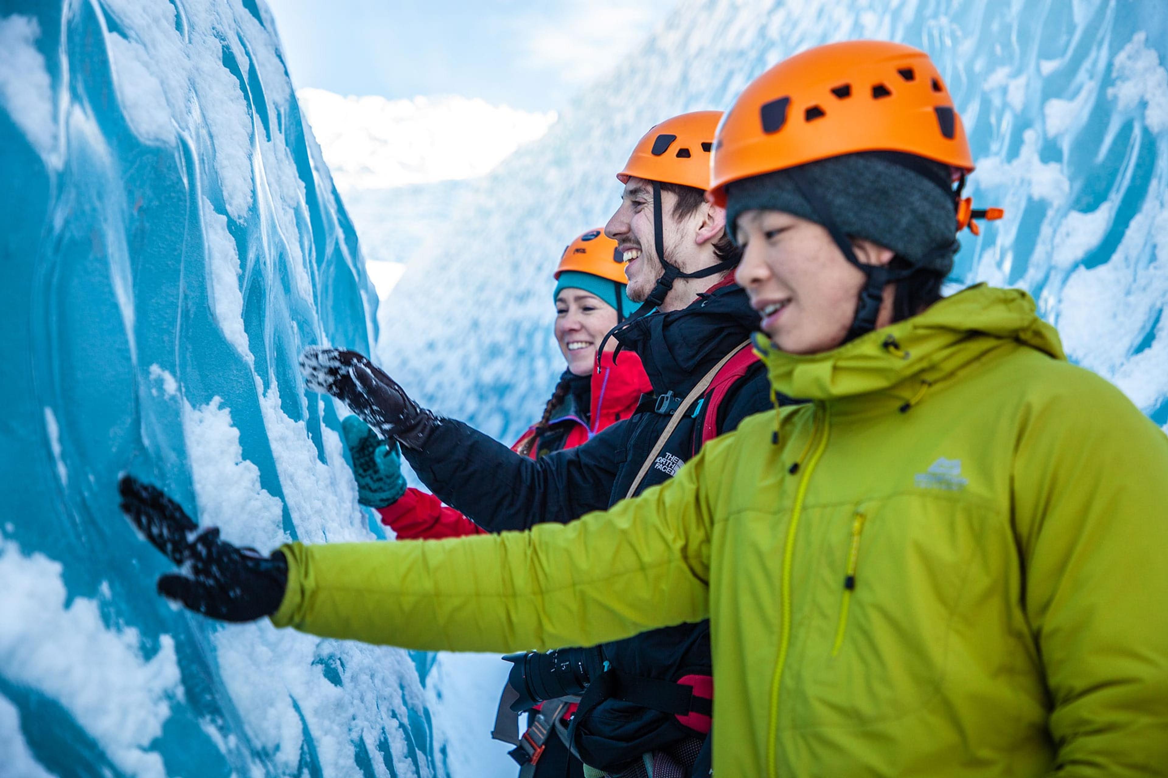 A man in a green jacket touching the blue ice in a crevasse on a glacier