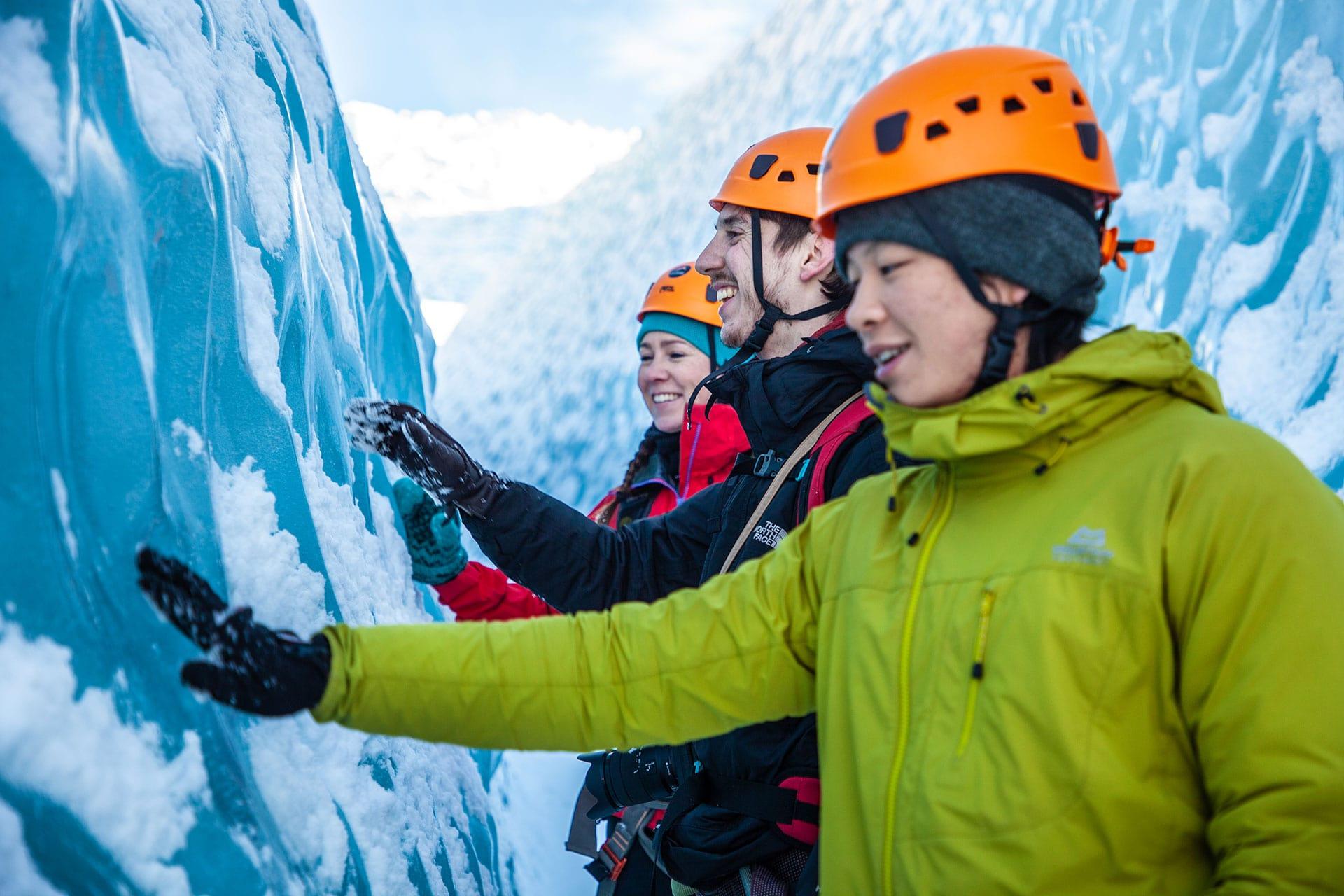 A man in a green jacket touching the blue ice in a crevasse on a glacier