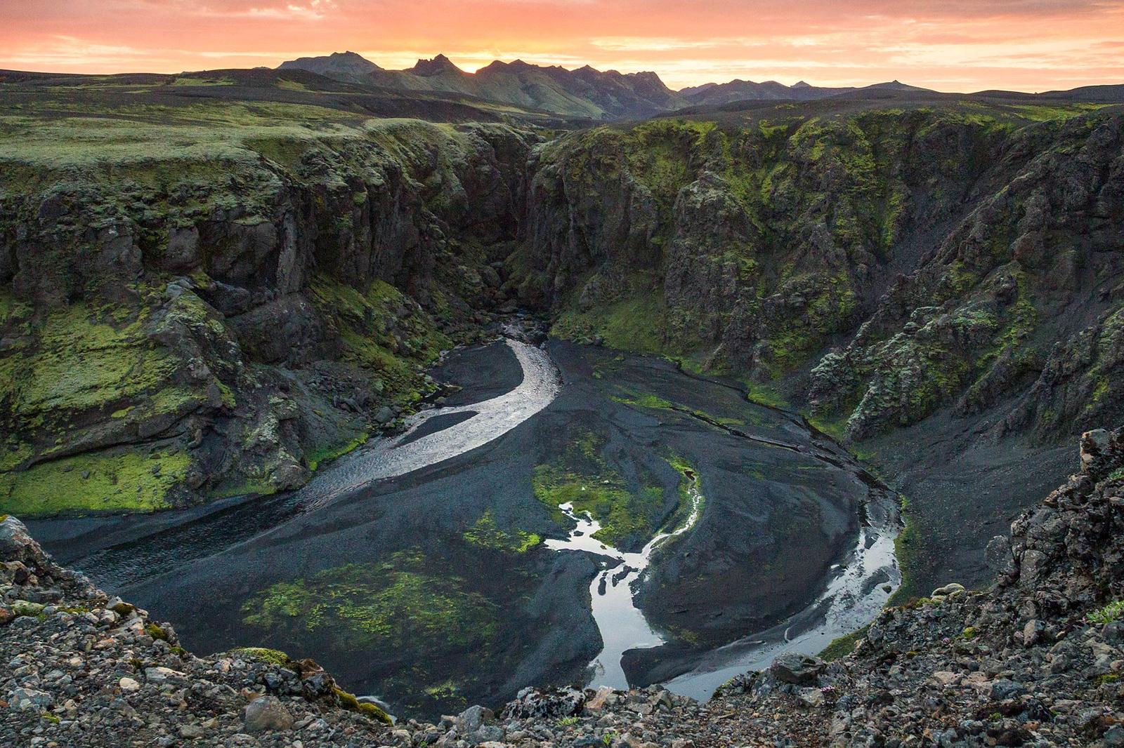 A beautiful scenery over a black mountain valley with nature growth and rivers running through it under the orange night sky