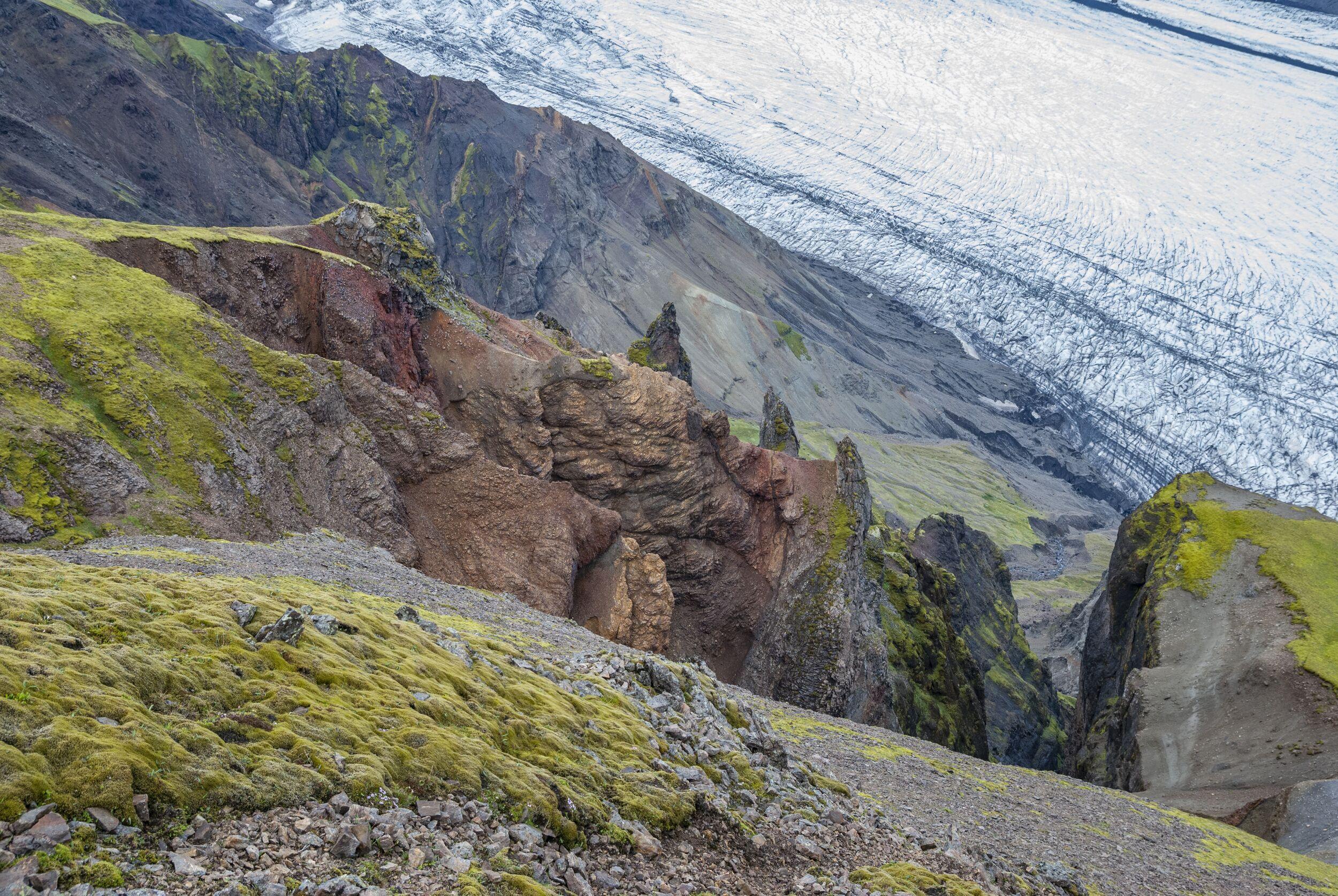 Green moss-covered terrain contrasting with icy glacier slopes along the Kristínartindar route.