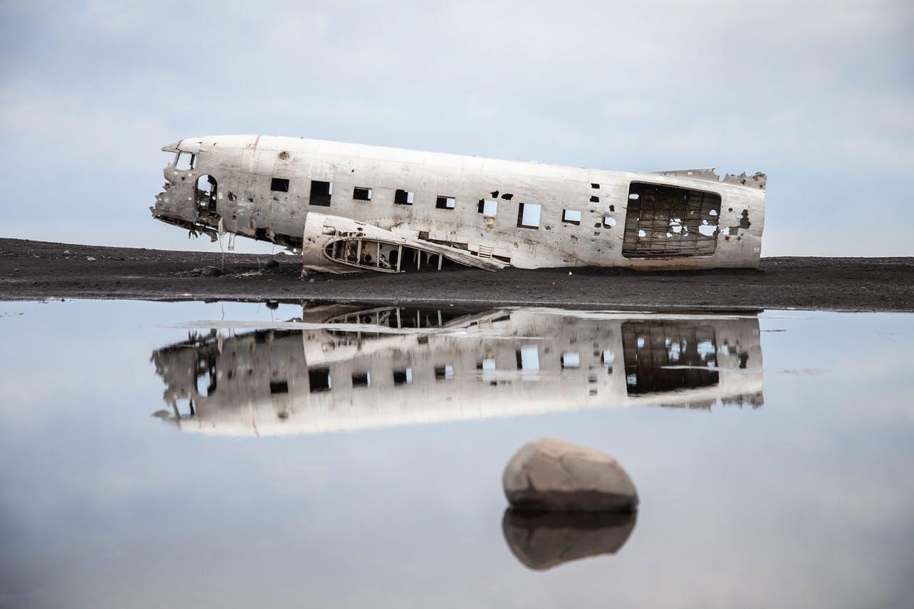 Plane wreck on black sand with water in the foreground