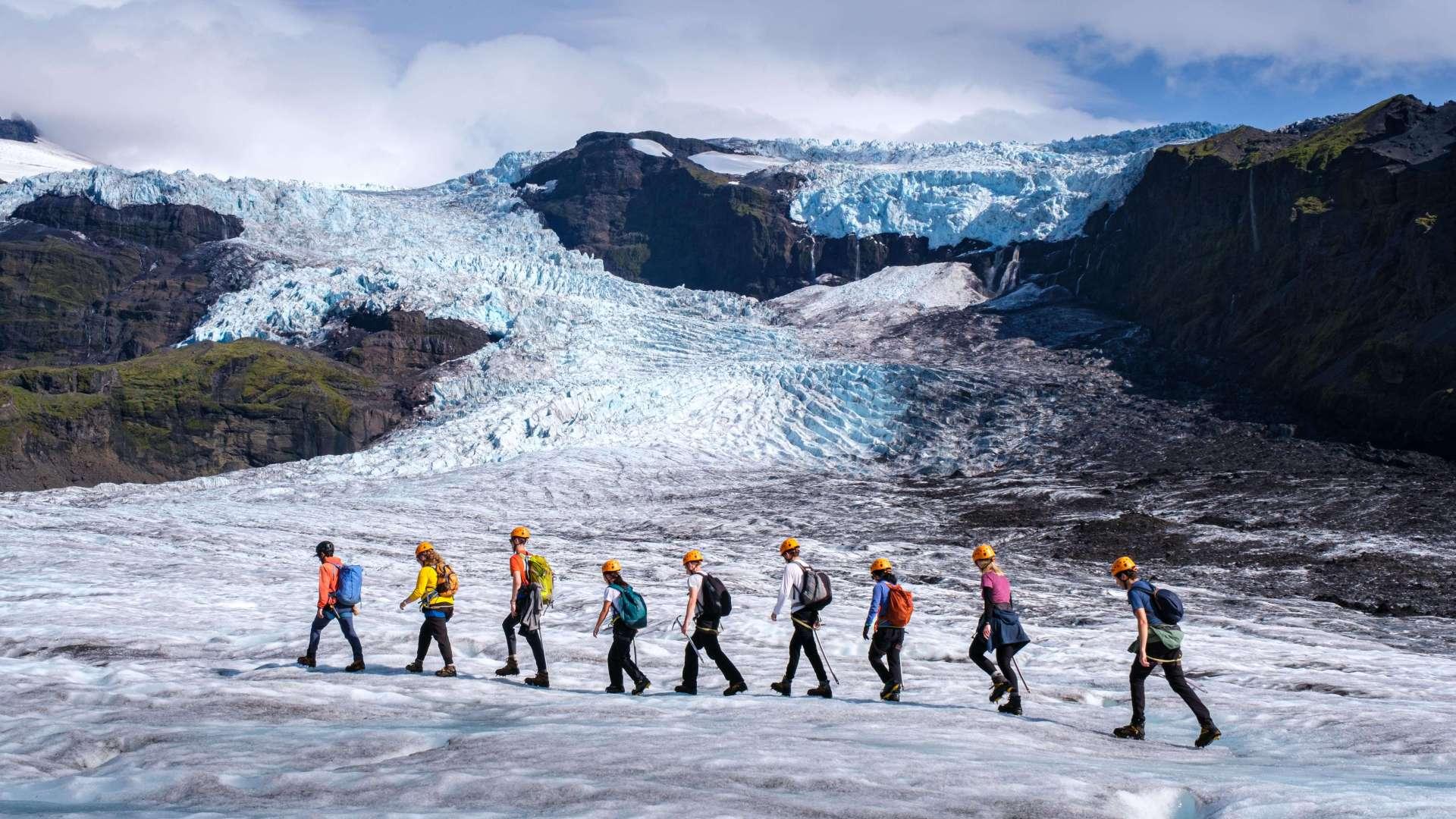 A group of people hiking over Virkisjokull glacier with the ice fall in background