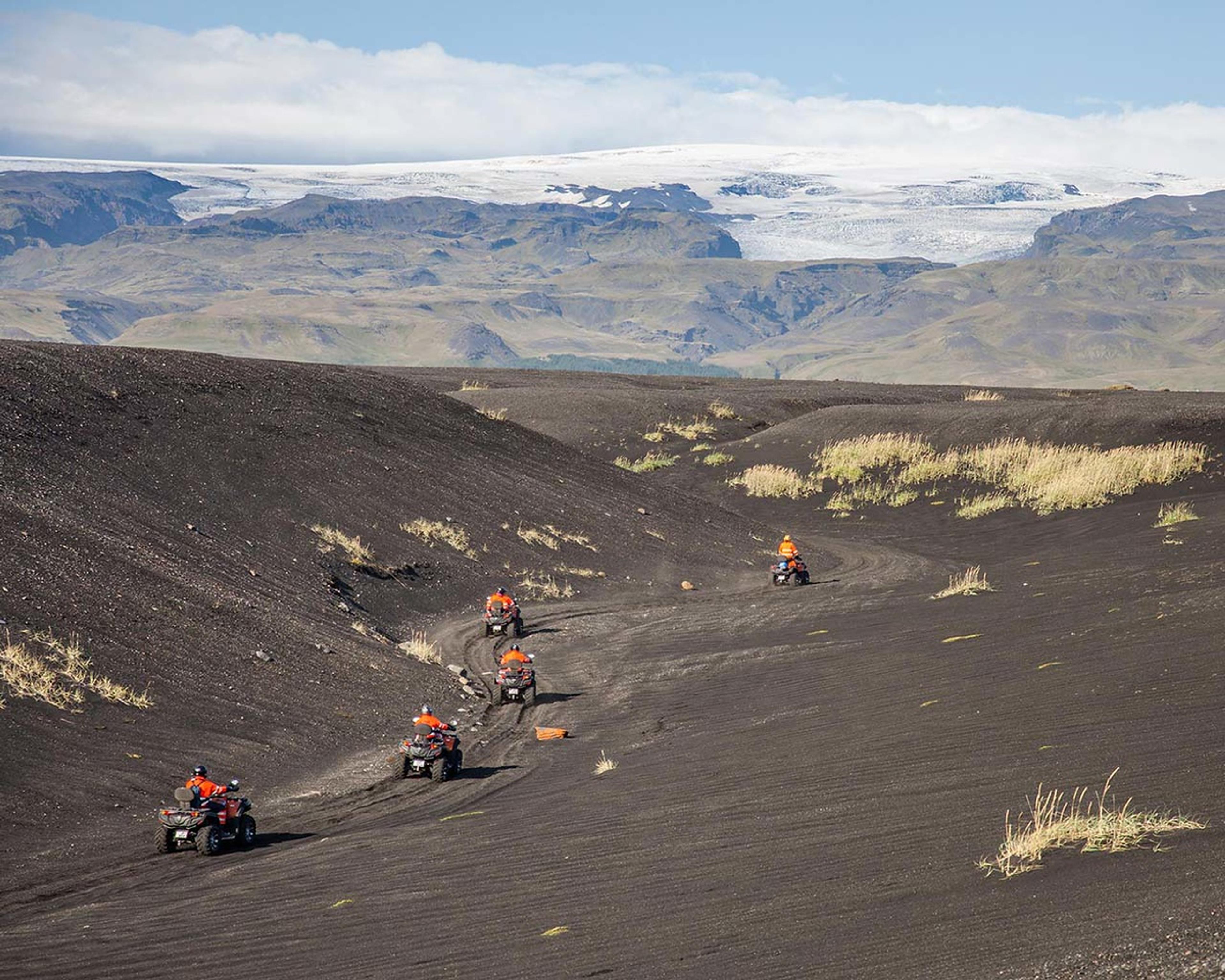 ATV quad bikes driving a winding track alond sand dunes and the glacier above