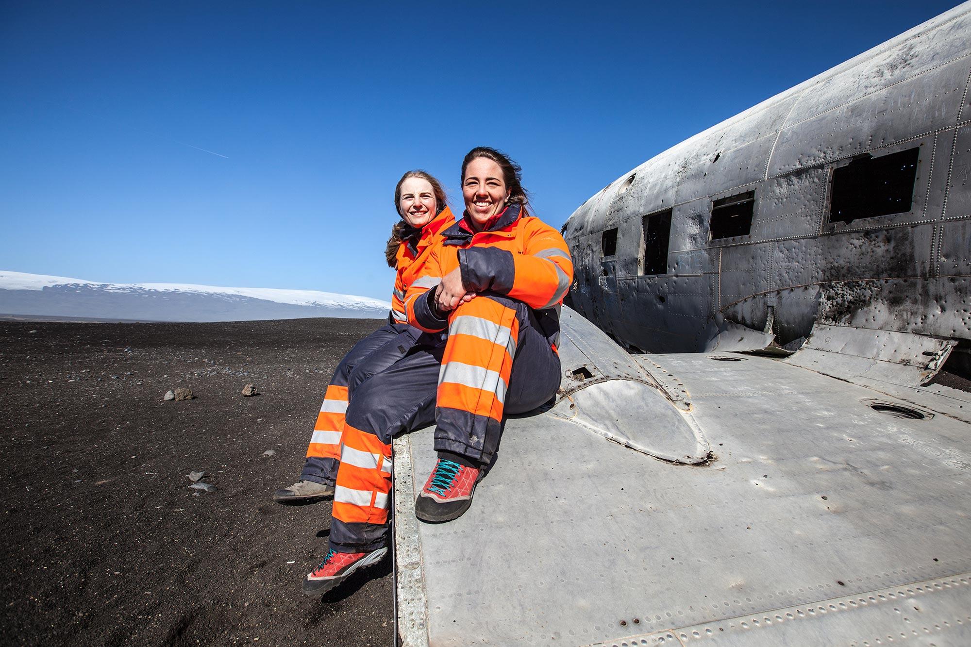 Two girls sitting on the wing of an old C-47 plane wreck on Sólheimasandur black sand area