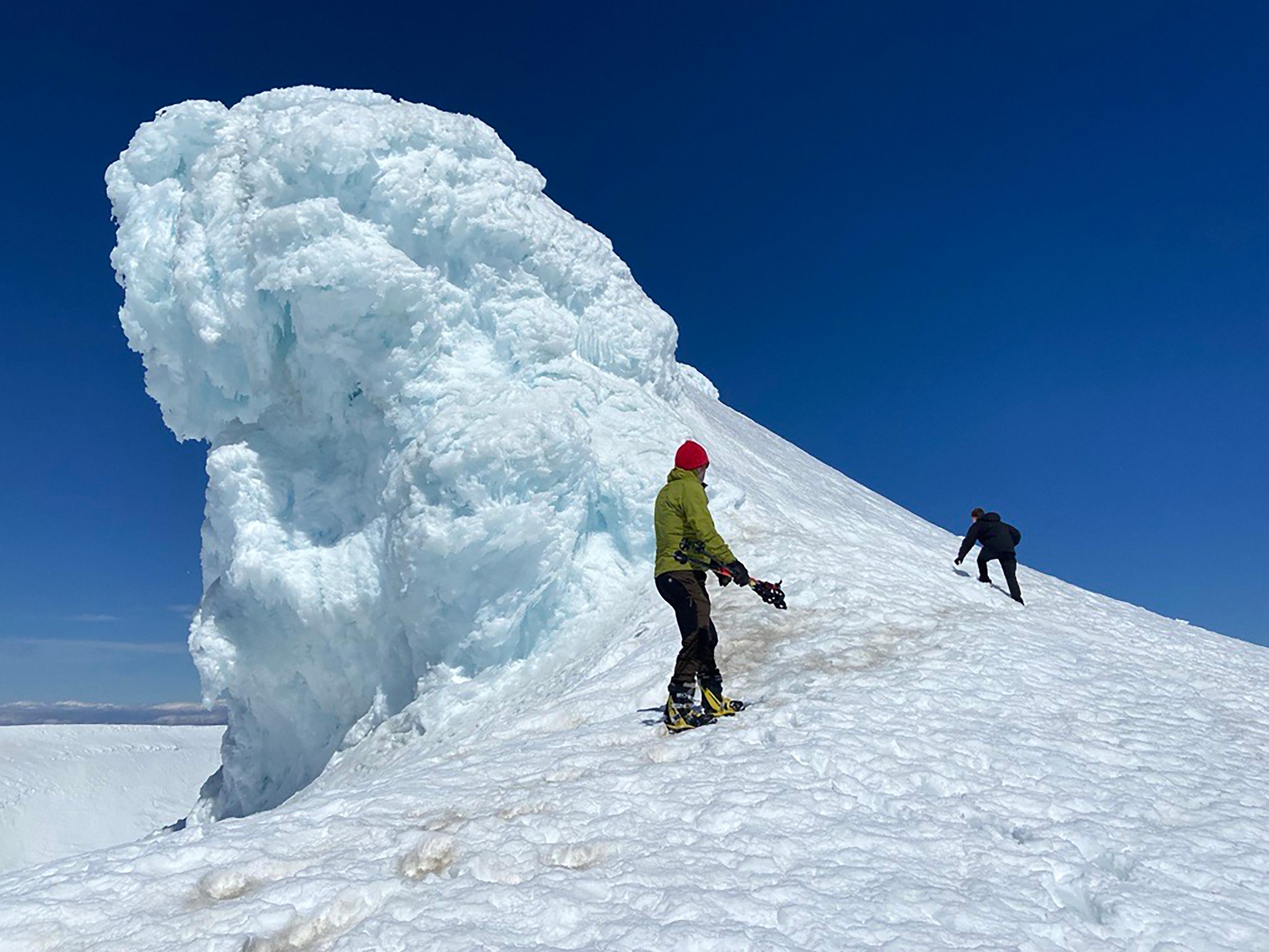 A group of six hikers, equipped with climbing gear, stands together on the snowy summit of Eyjafjallajökull glacier under a bright, clear sky.