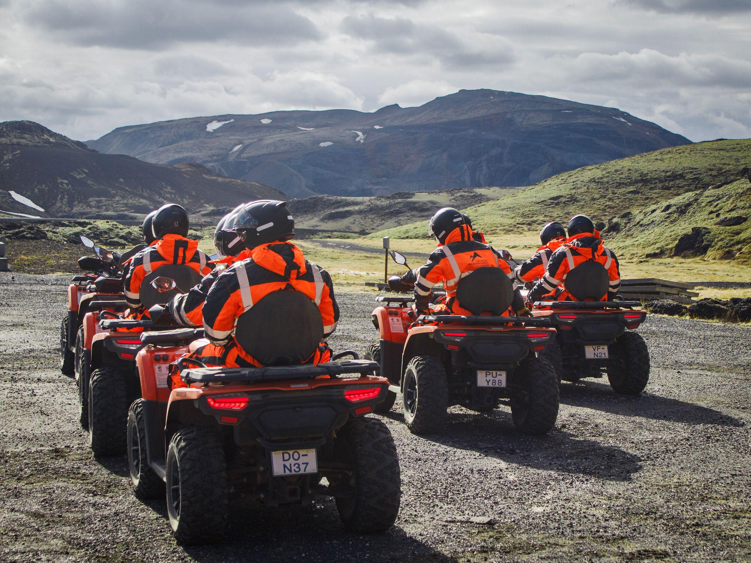 five people riding atv on a gravel road with a green hill and a mountain