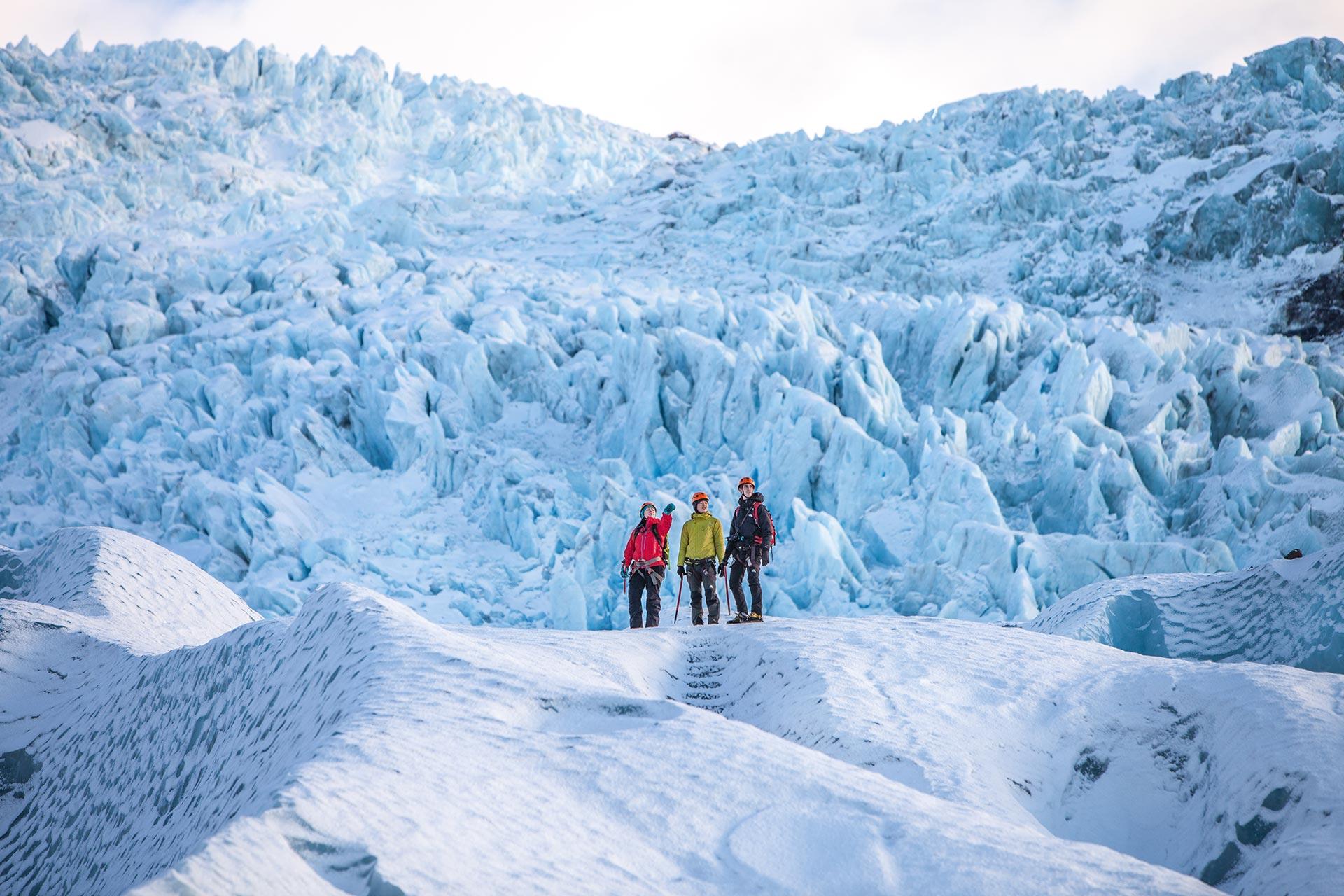 A guide in a red jacket from Icelandic Mountain Guides stanidng along with two clients with an awesome ice fall in the background