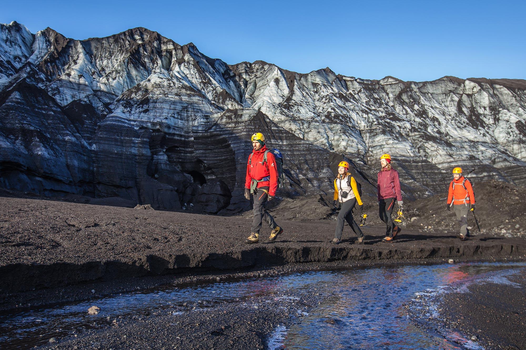 People walking on black sand with black mountains in the back and a bright blue sky