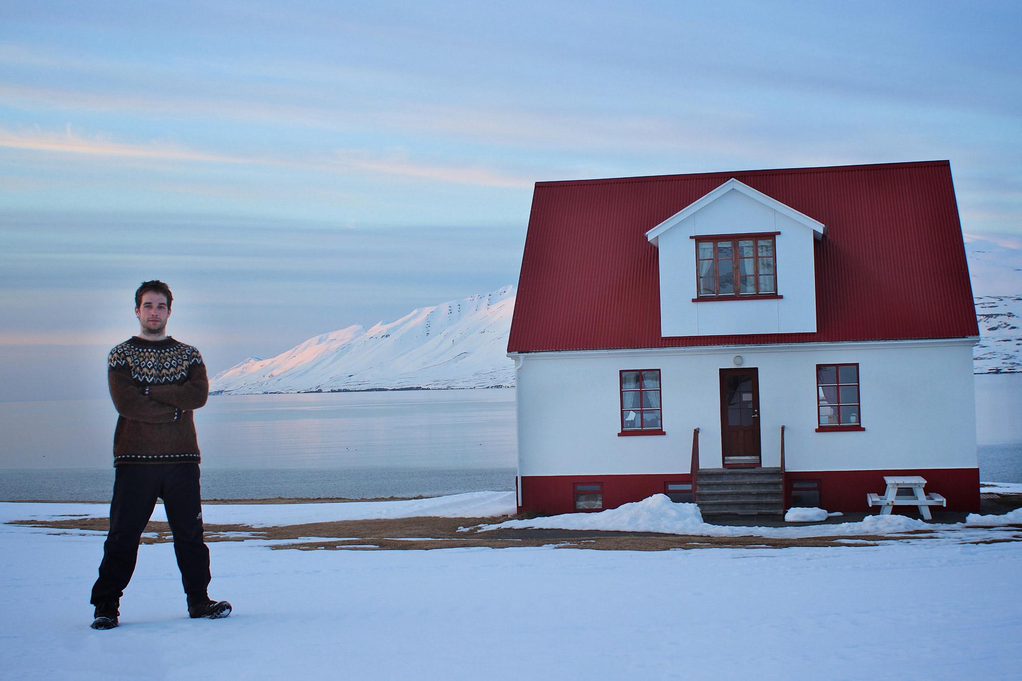 A man in an Icelandic sweater standing next to a small, cozy hut in a snowy winterland in the north of Iceland