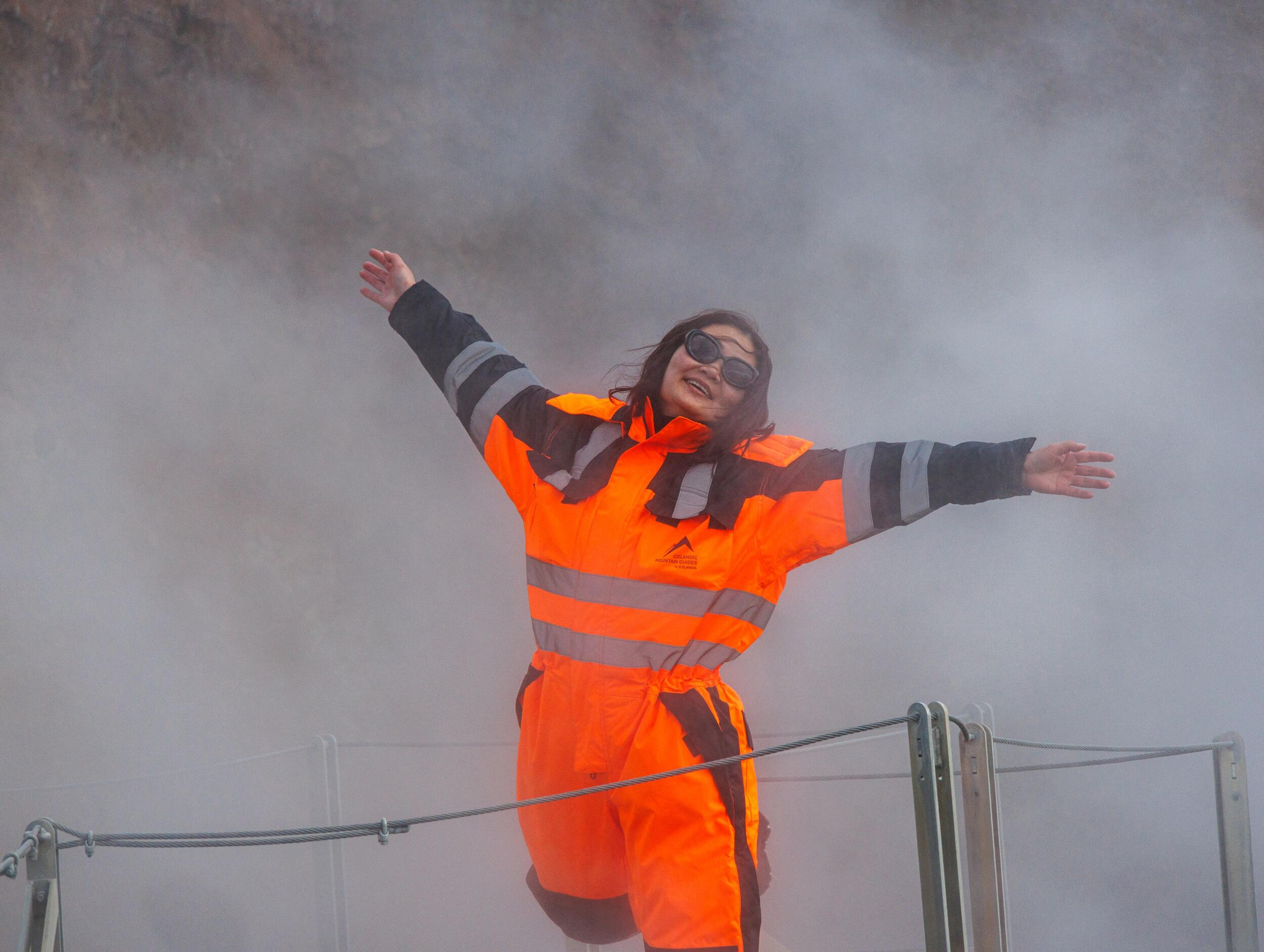 Smiling woman in ATV overalls standing in a cloud of steam.